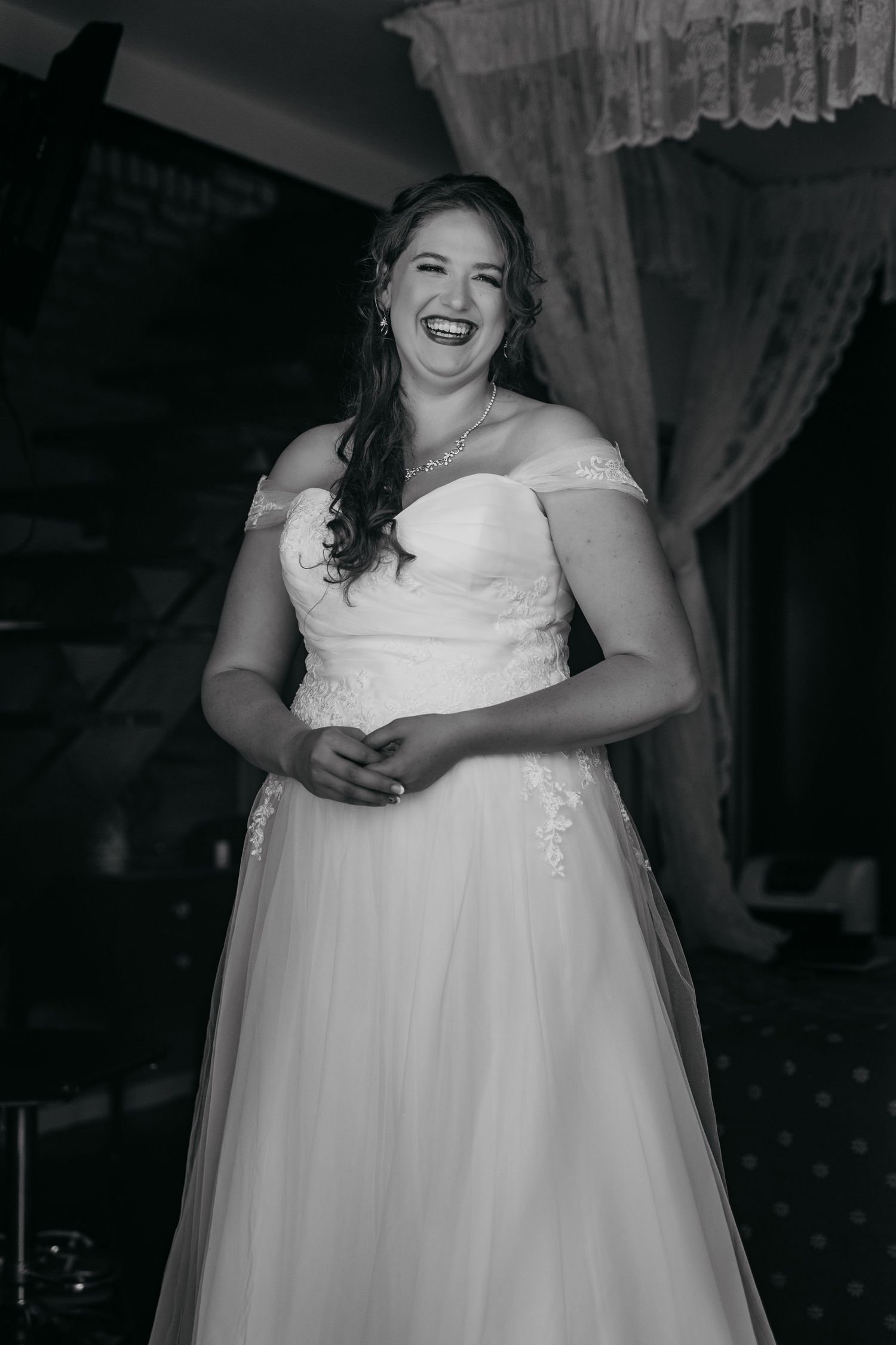 A smiling bride in a white off-shoulder ballgown poses in black and white photography.