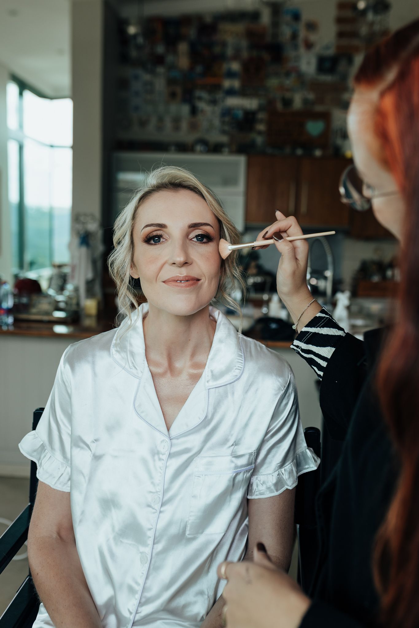 Makeup artist applying cosmetics to guest wearing white silk robe during preparation session.