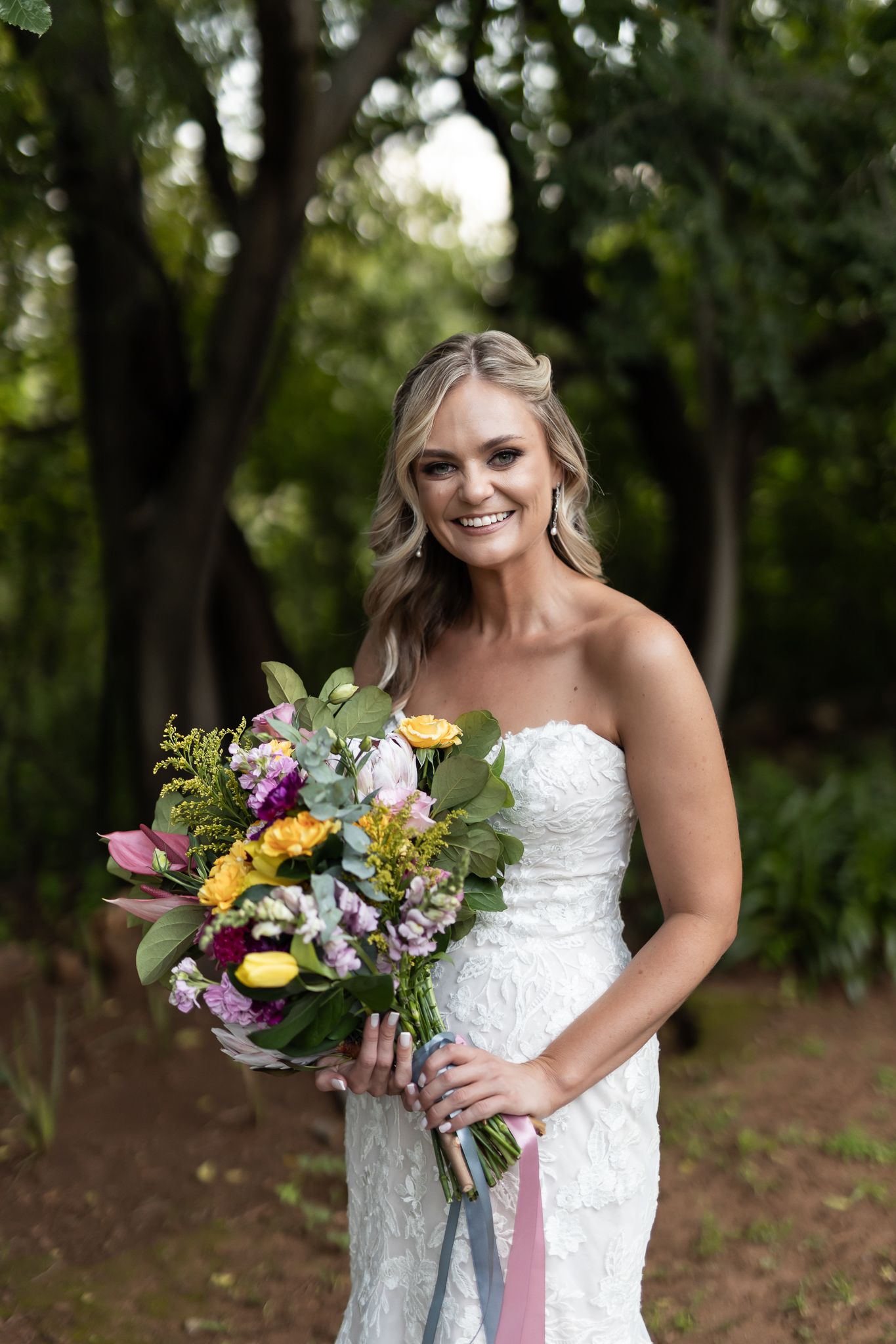 An elegant bridal portrait showcasing a strapless white gown and colorful bouquet in a garden setting.