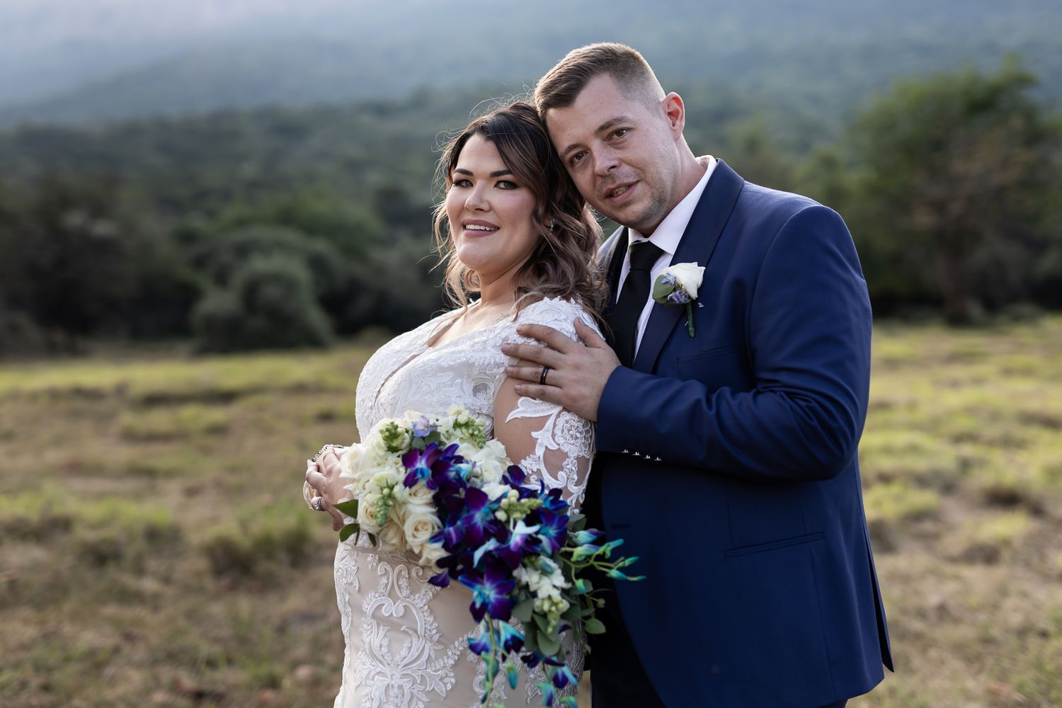 Intimate wedding portrait with blue and white floral bouquet against mountain landscape.