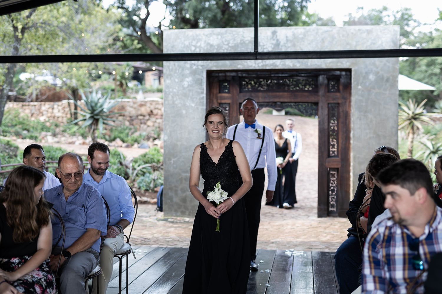 Wedding ceremony guest procession on wooden deck with ornate doorway in background.