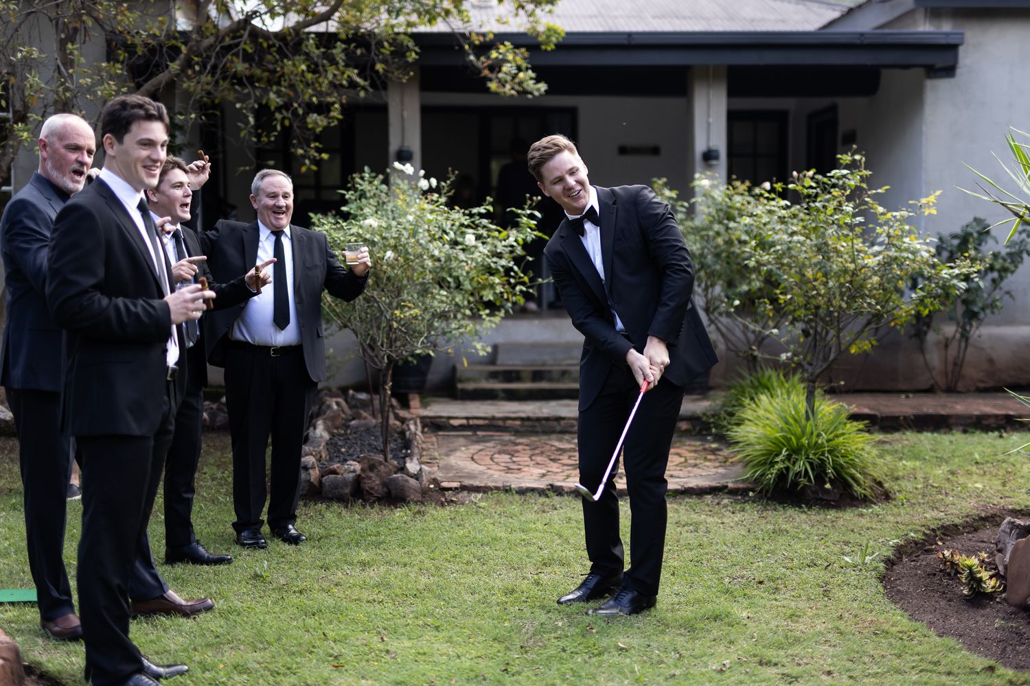 Group of formally dressed people laughing on lawn while one person bends over.