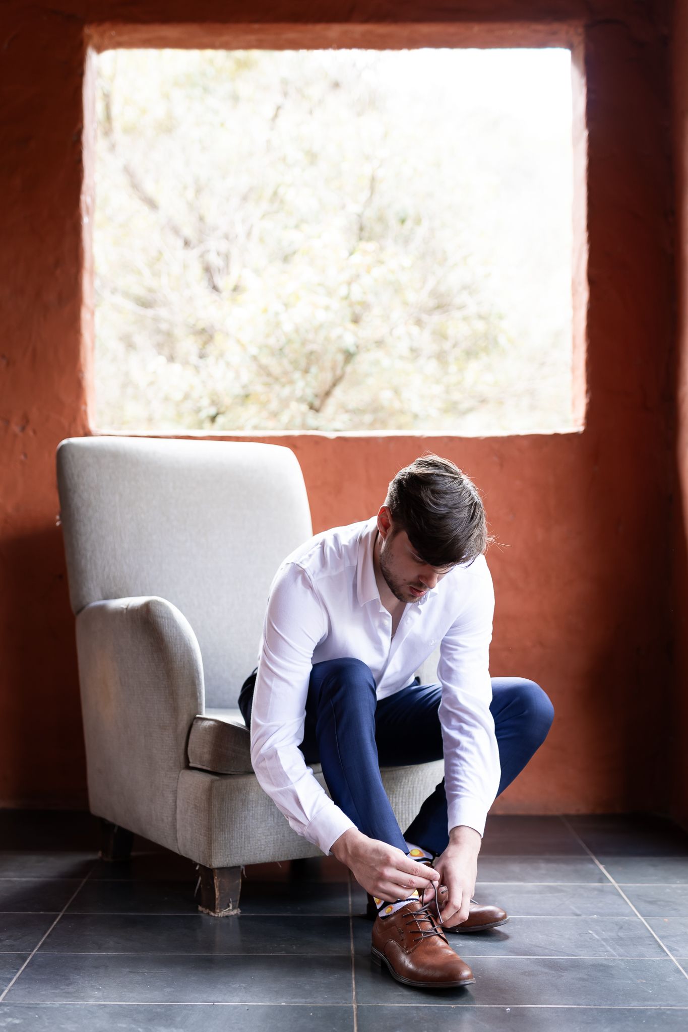 Chair and window scene with brown dress shoes and formal attire.