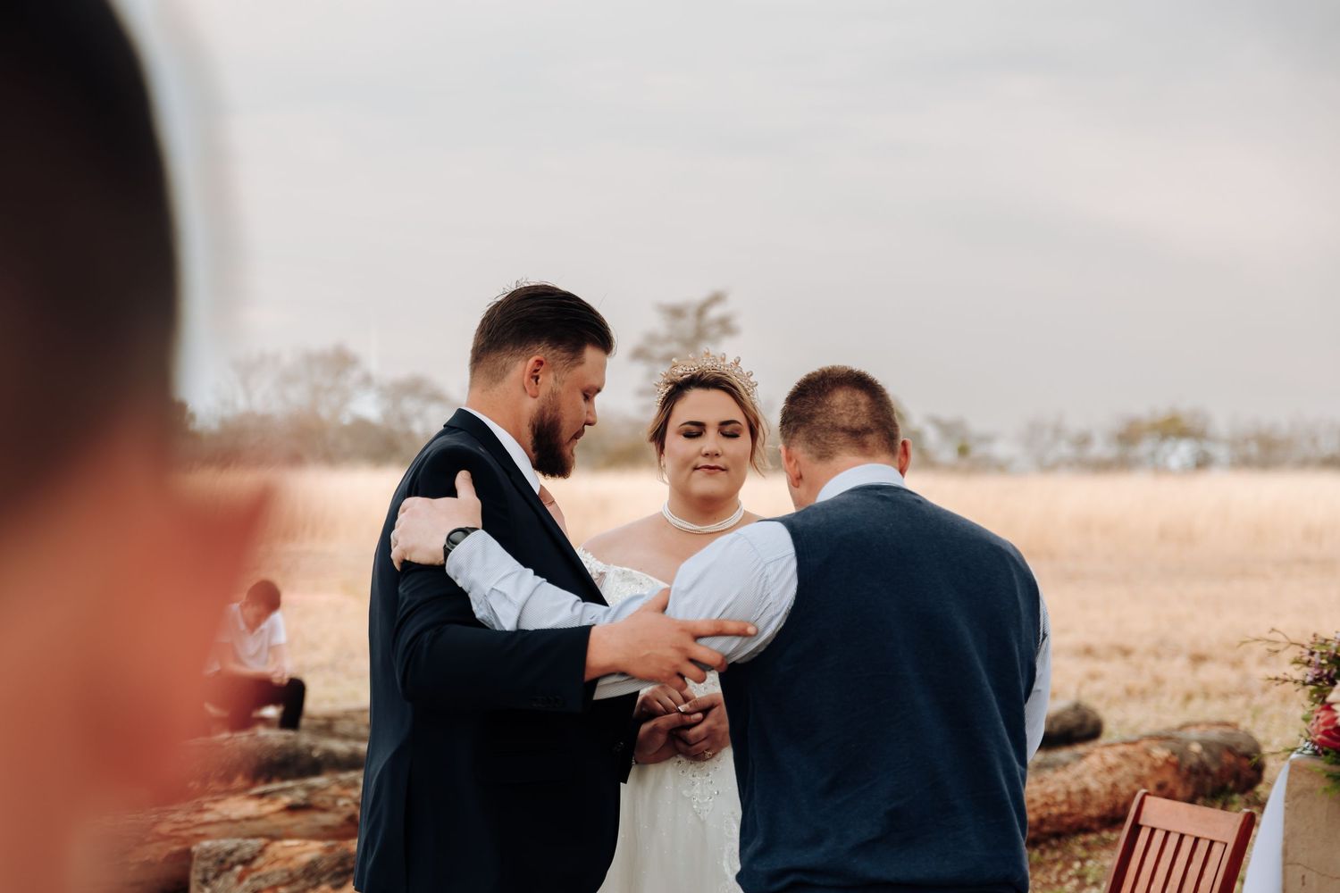 An intimate outdoor wedding ceremony takes place on a hilltop with blurred background scenery of distant trees and fields.