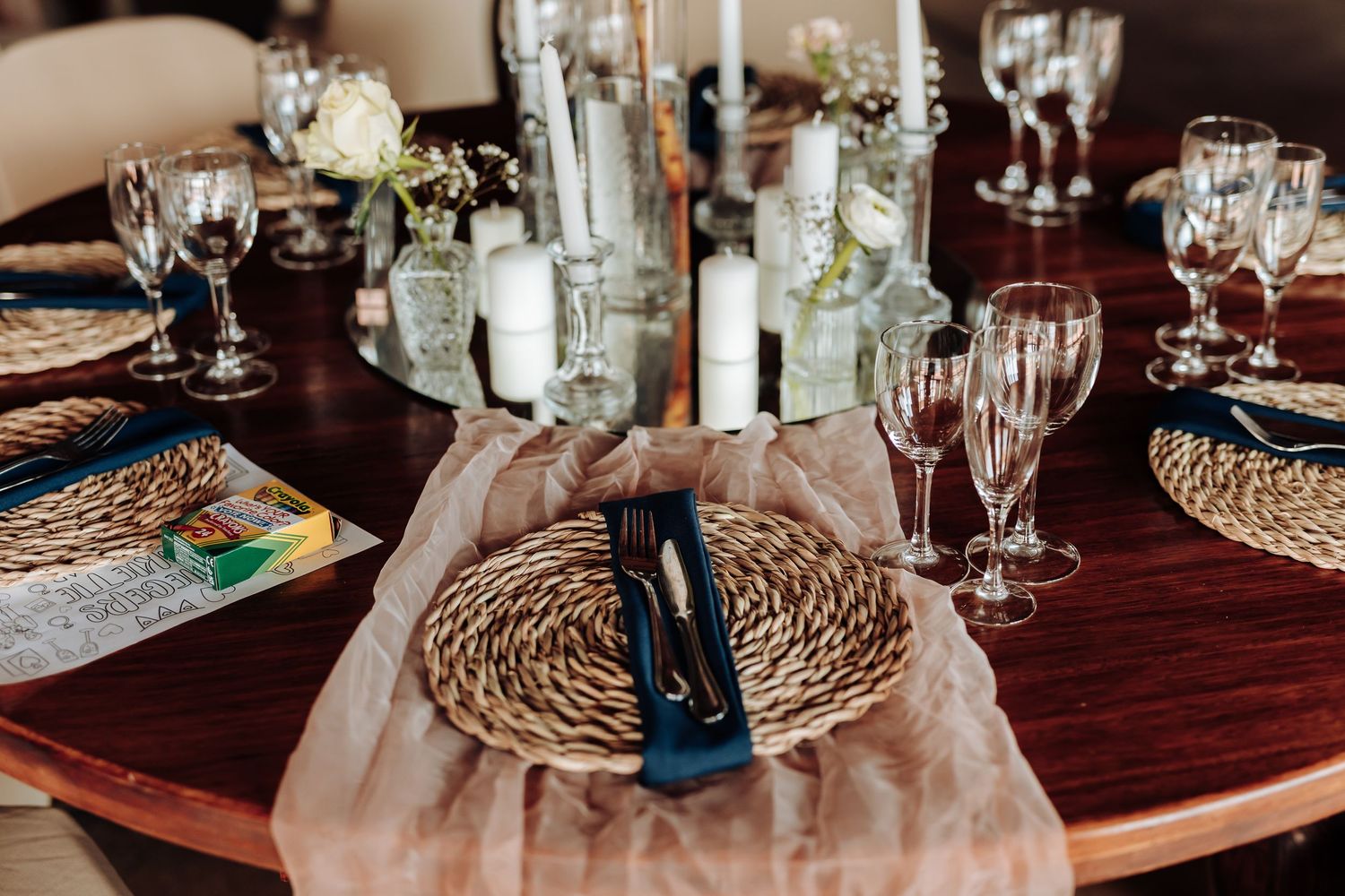 Elegant table setting with woven charger plates, crystal glasses, and white floral centerpieces on a dark wood table.