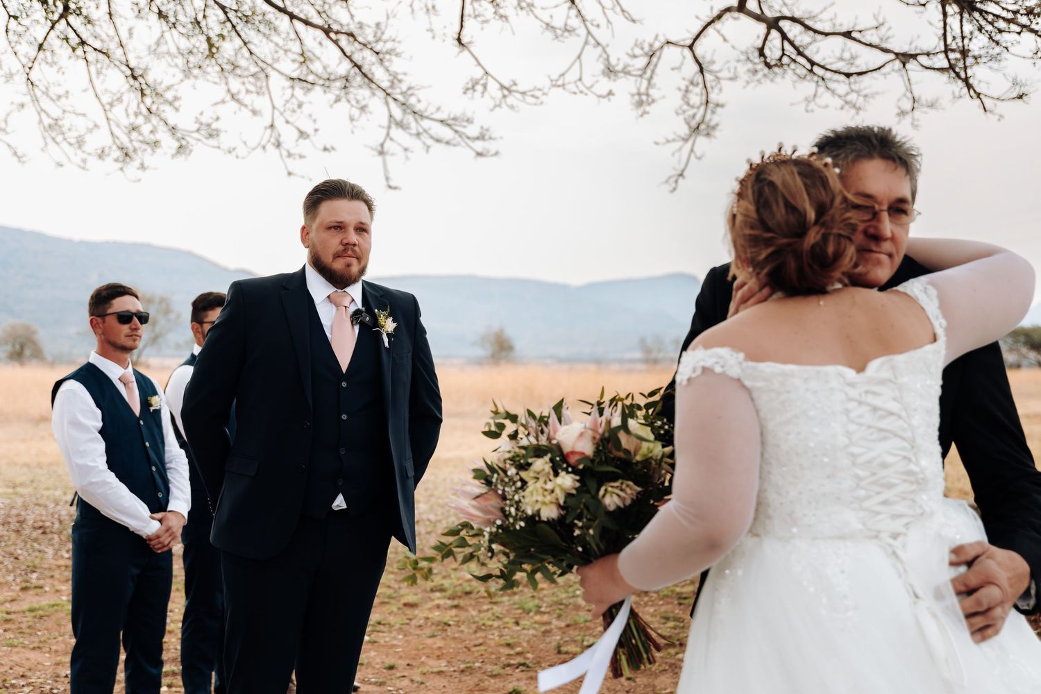 Emotional outdoor wedding ceremony moment during autumn in a mountainous field with a lace dress and black suit.