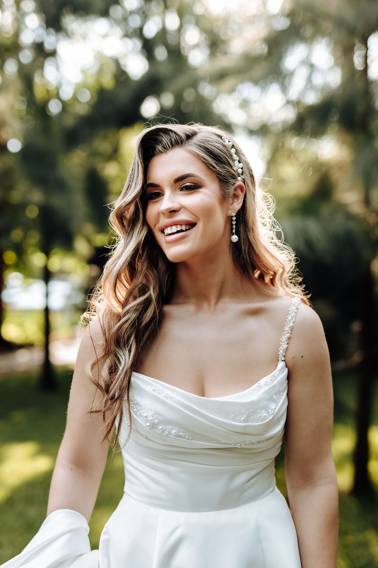 A white wedding dress shimmers in natural sunlight against a dreamy outdoor backdrop.