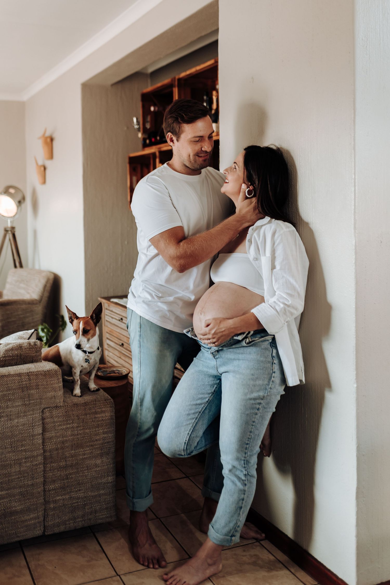 Intimate couple photoshoot against white wall showing playful poses in casual denim and white outfits.
