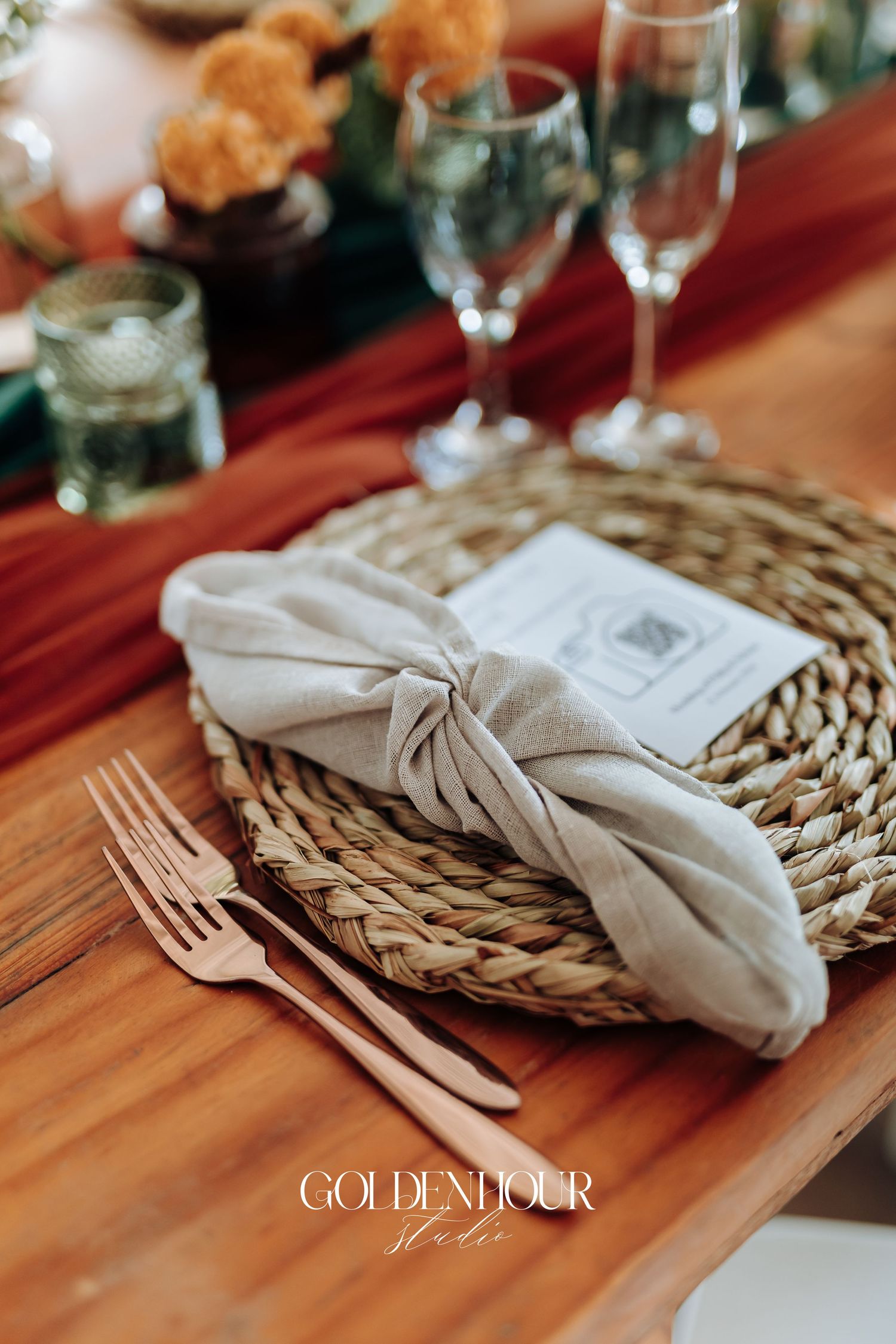 Rustic place setting with woven placemat, linen napkin, and wooden table at an elegant wedding reception.