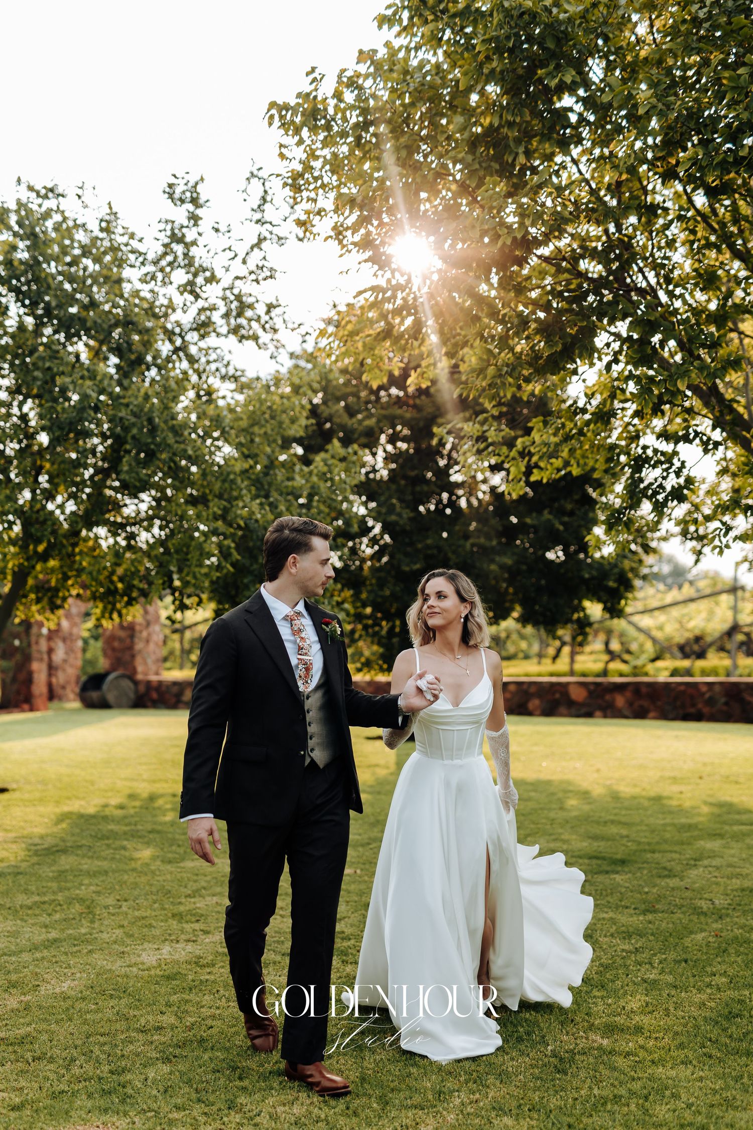 Bride and groom share romantic moment in sunlit garden setting.