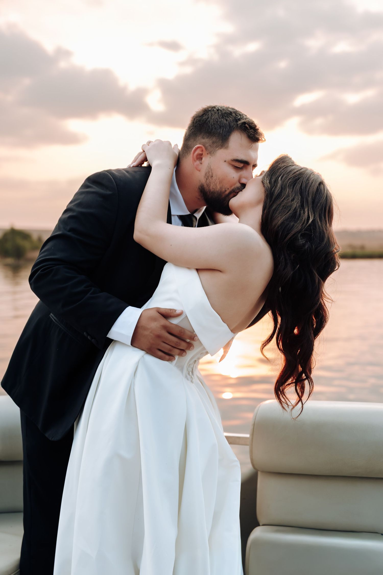 Romantic couple embracing and kissing on a boat during sunset over calm waters.