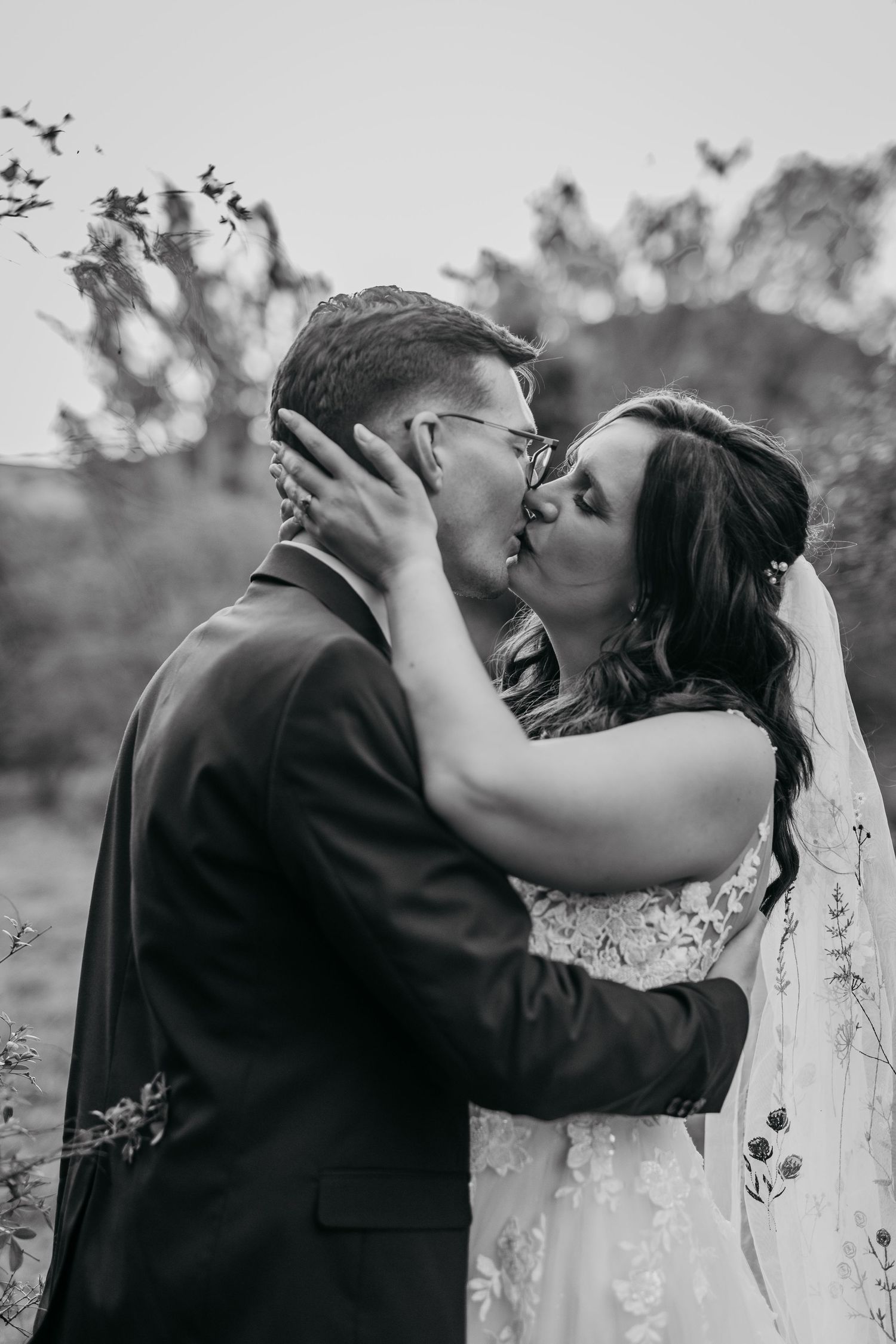A romantic black and white wedding photo captures a tender kiss between newlyweds in an outdoor garden setting.