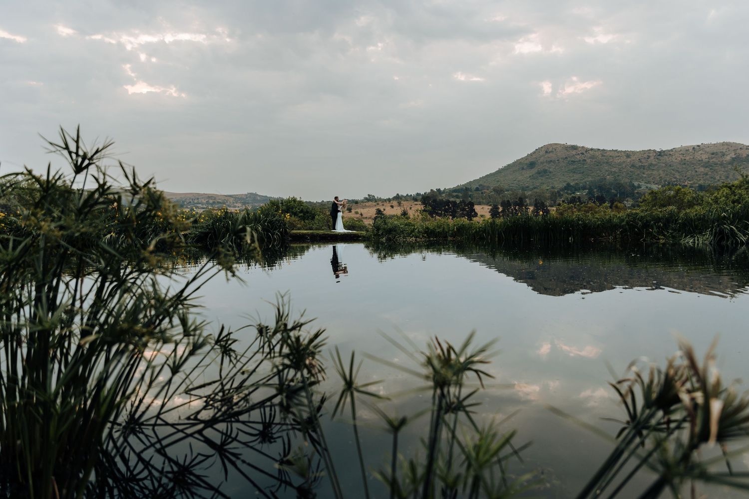 Panoramic view of a serene lake surrounded by mountains and trees reflecting in the calm water at dusk.