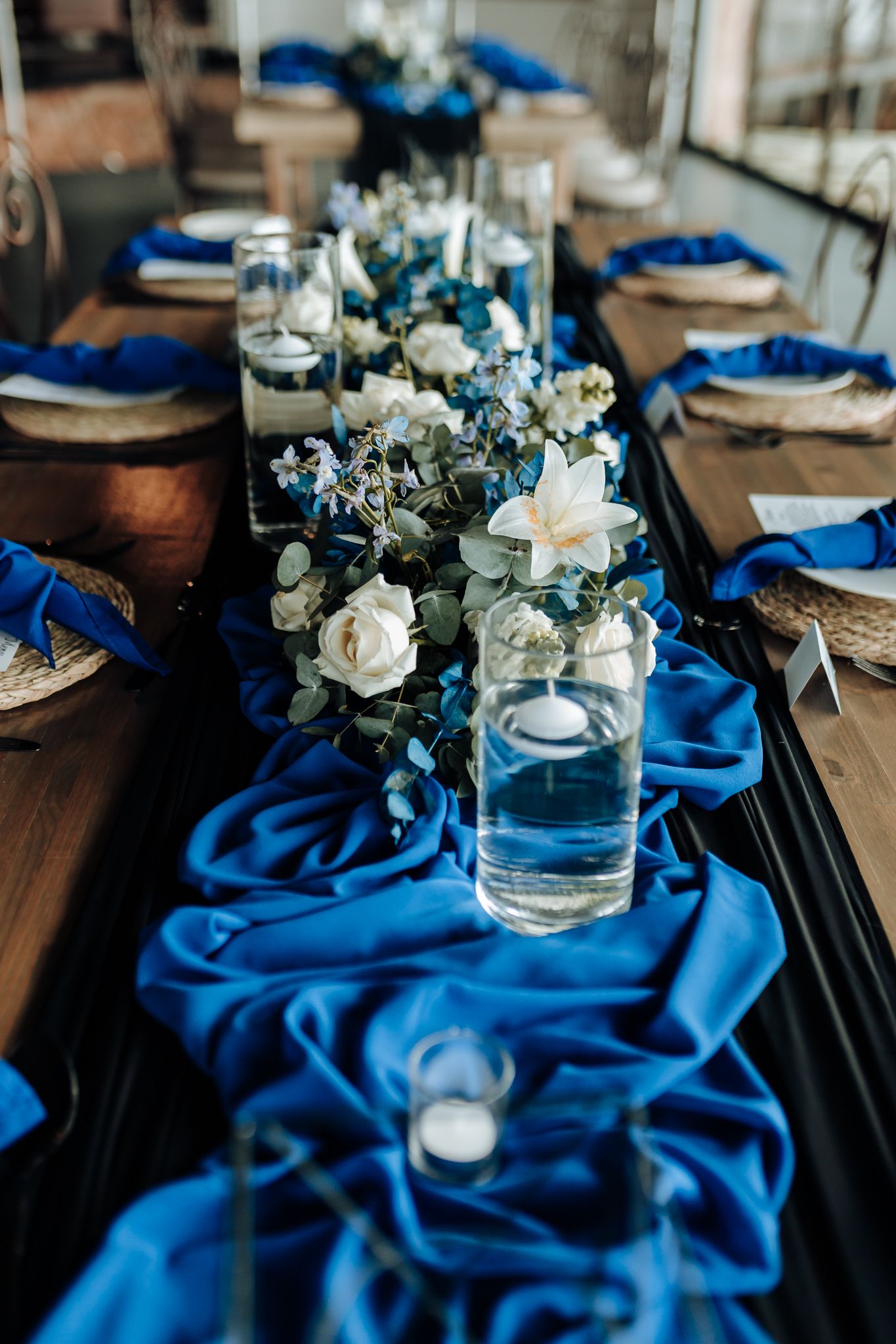 Wedding centerpiece with white roses and blue fabric table runner.