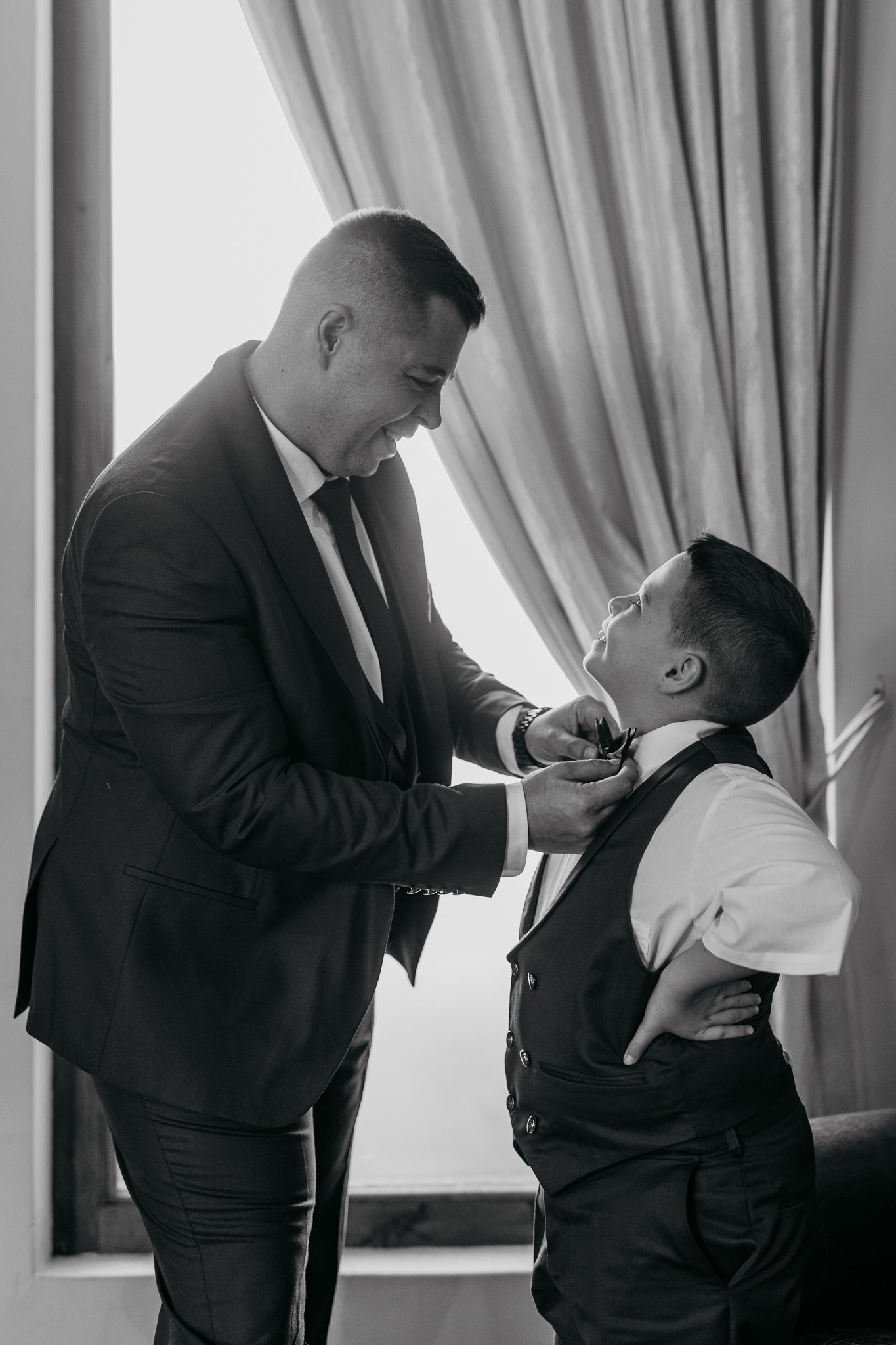 A touching moment between a man in a suit adjusting a young boy's bowtie before a formal event.