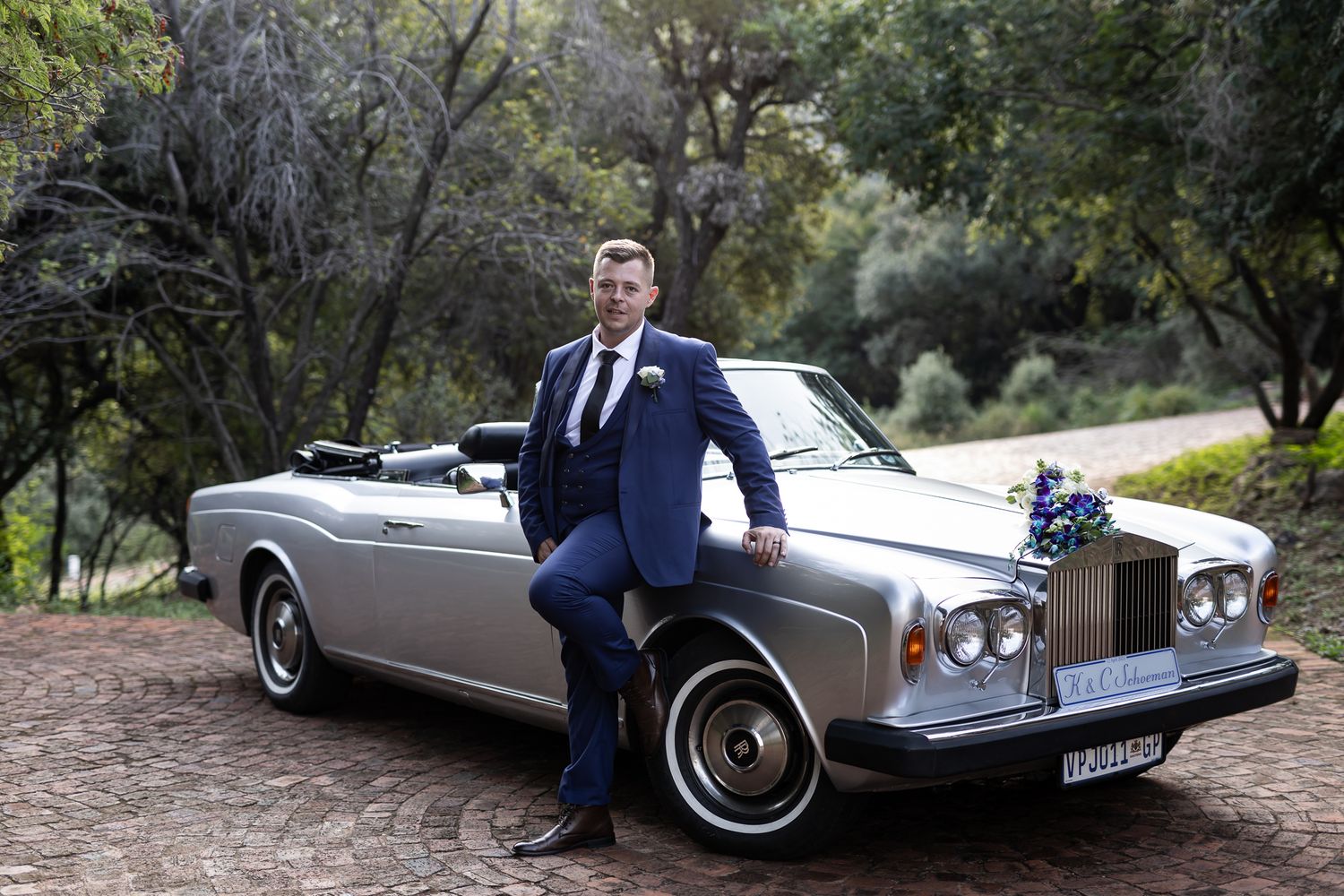 Groom in navy suit poses with vintage silver Rolls Royce convertible.