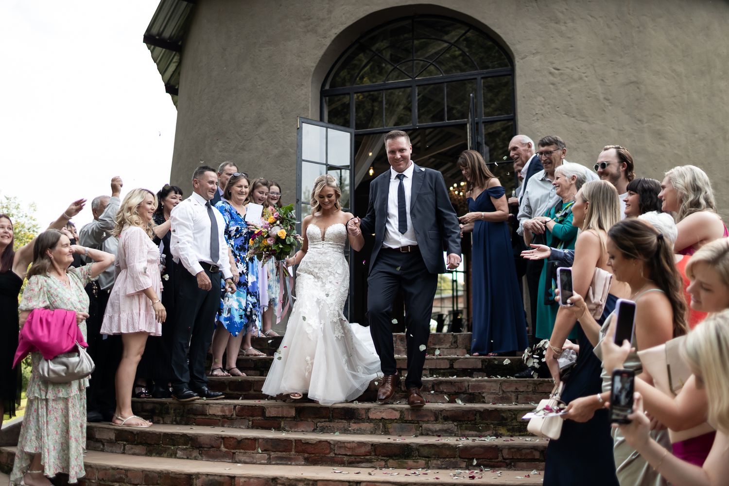Wedding guests shower confetti on newlyweds descending stone church steps.