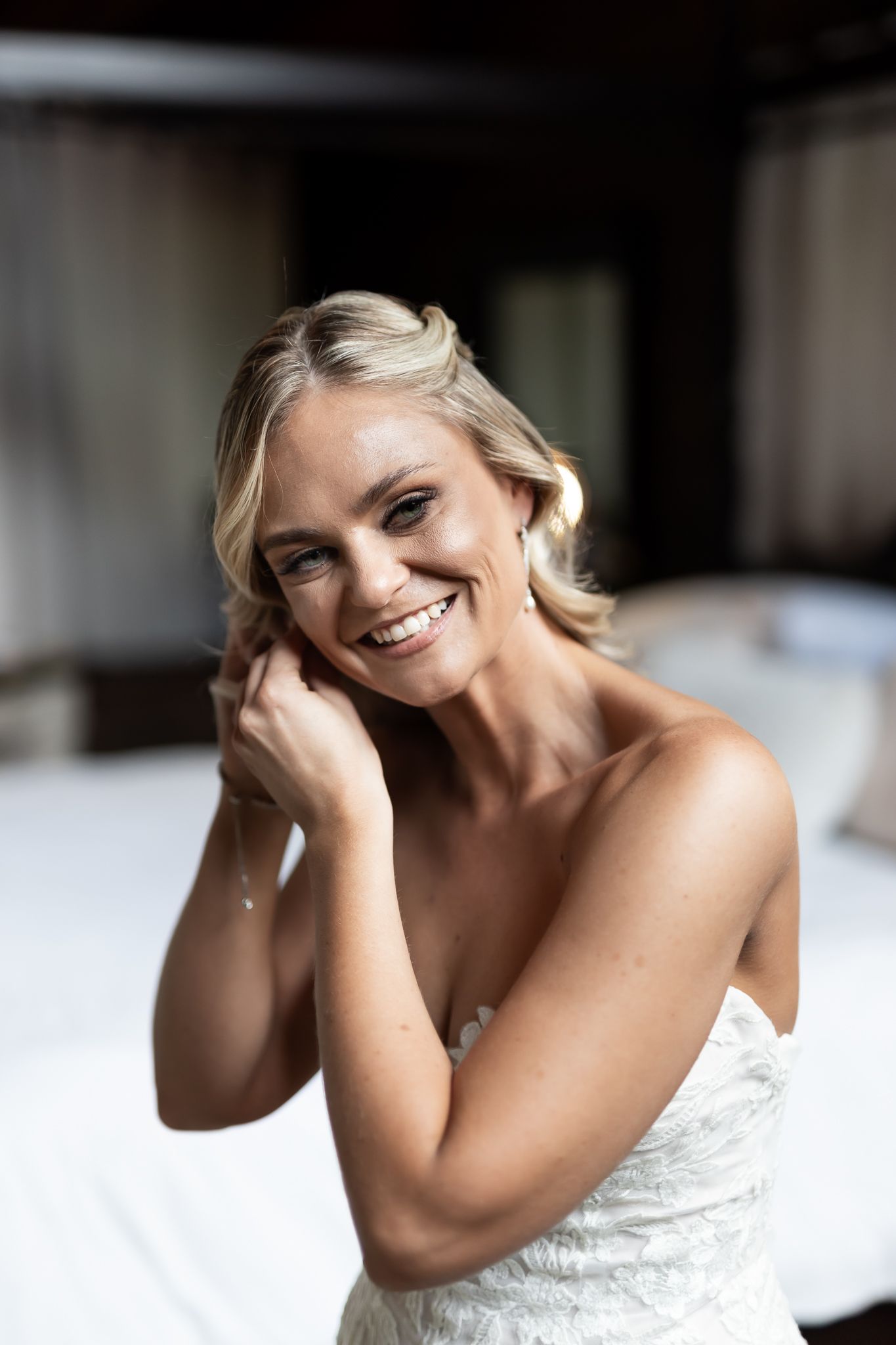 Beautiful bride in white lace gown smiles while touching her earring.