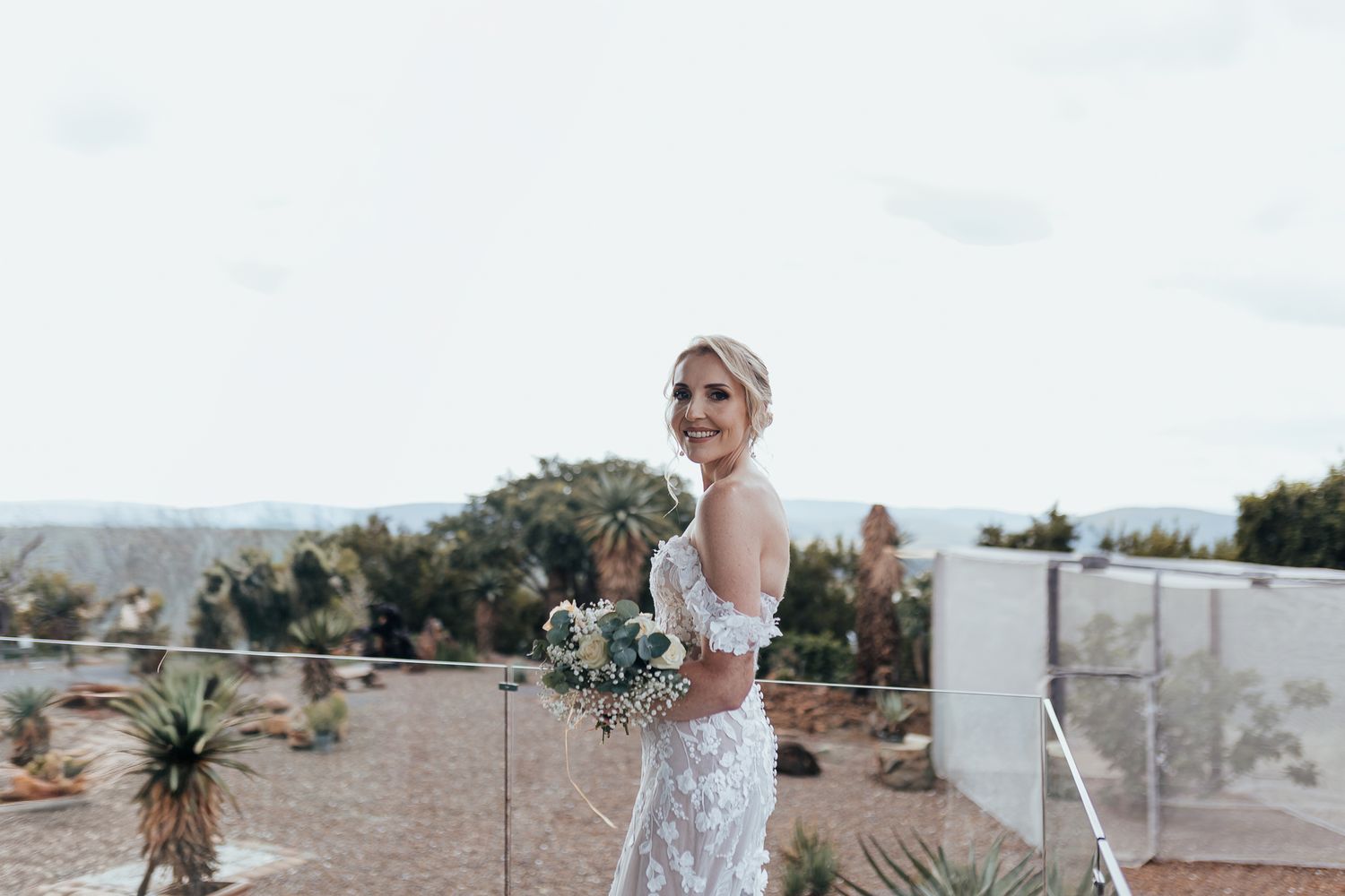 Bride holds bouquet while standing on outdoor deck with mountain views.