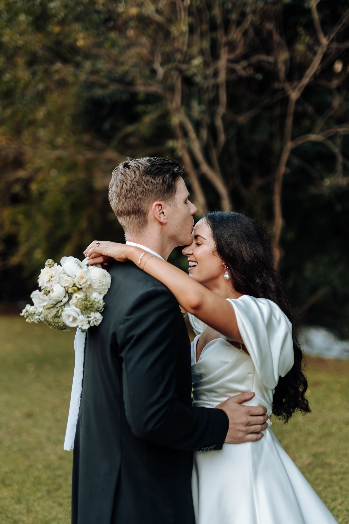 A romantic wedding embrace with white bouquet against autumnal outdoor setting.