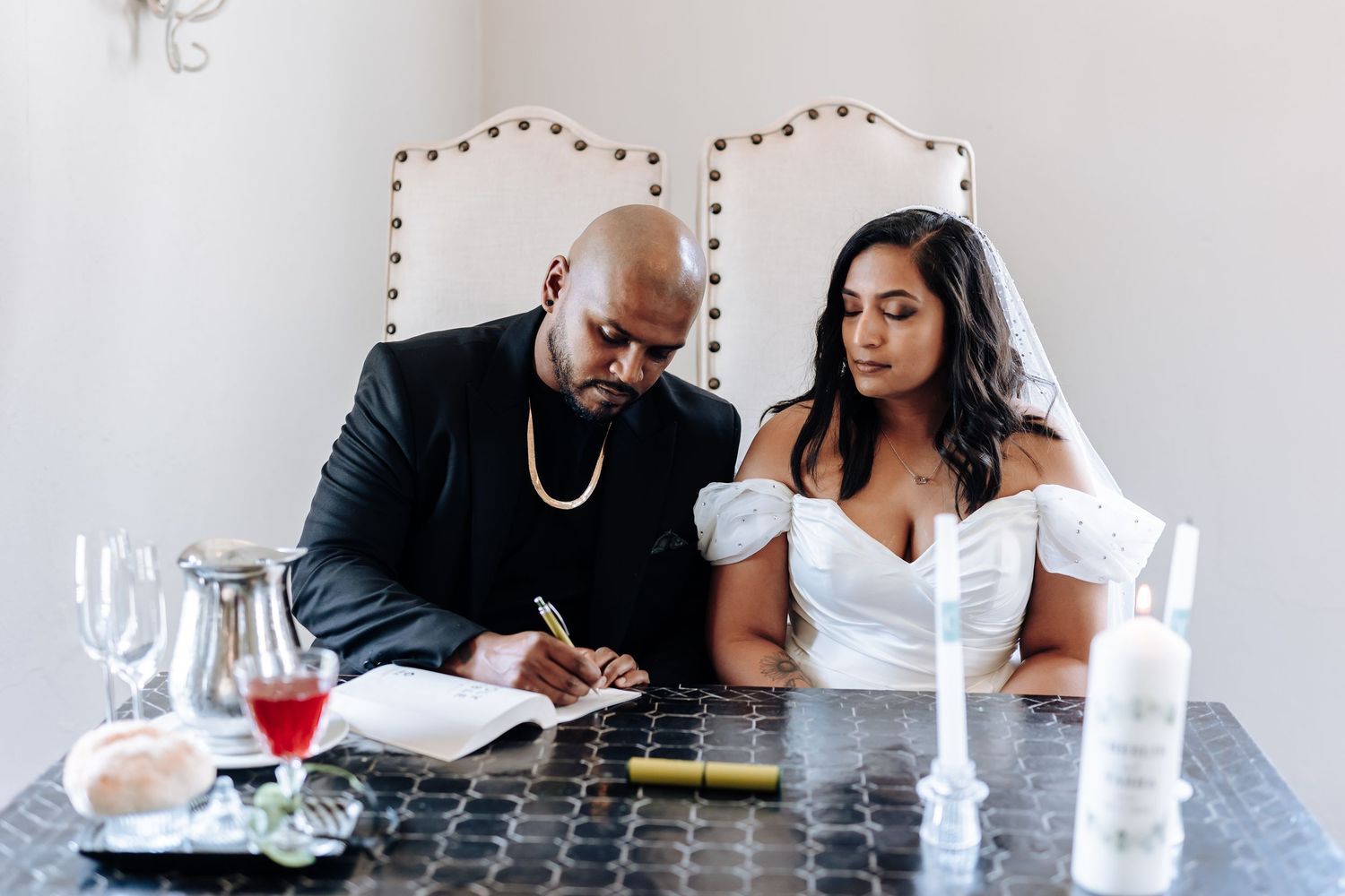 Bride and groom signing marriage documents at elegant table setting.