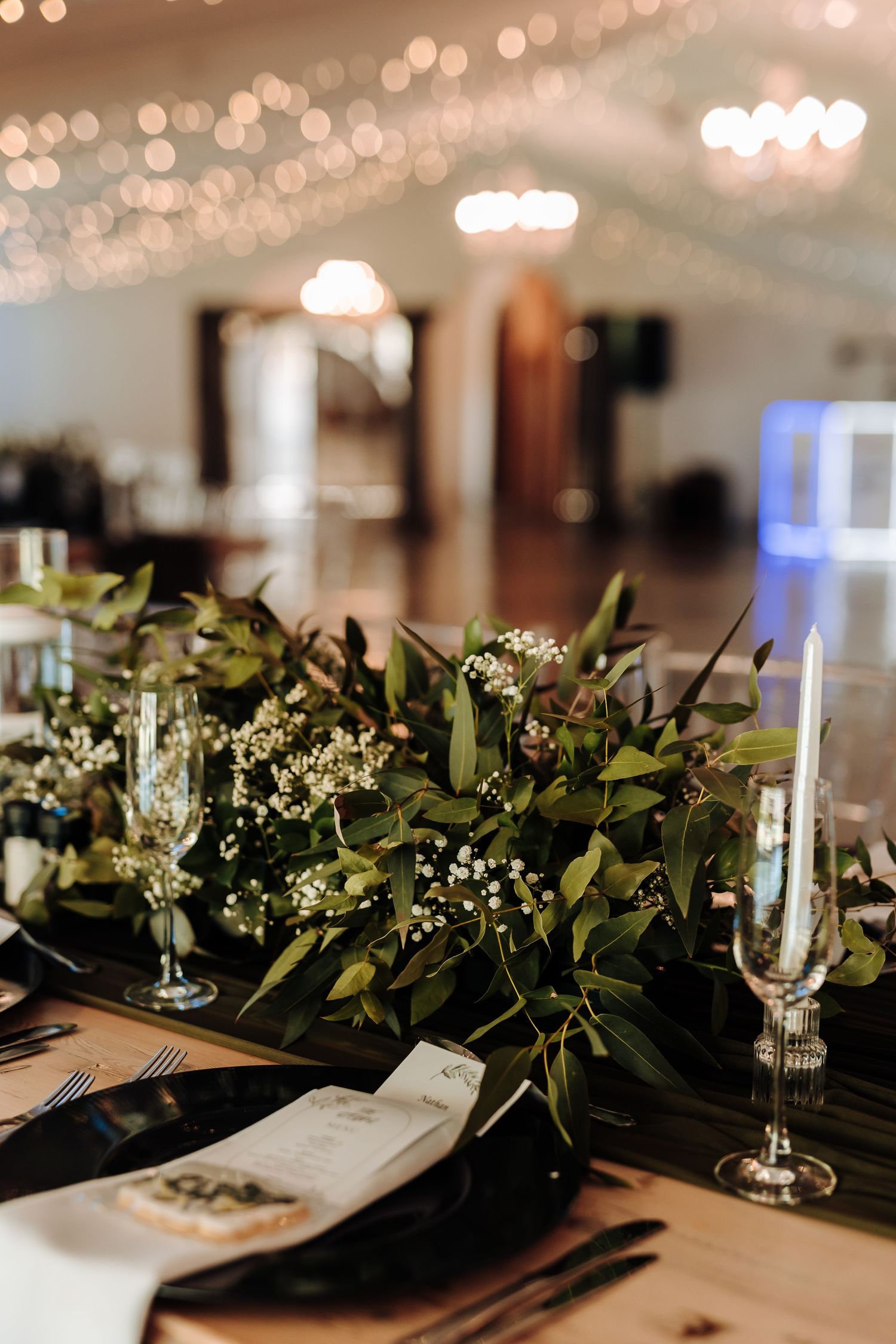 Luxurious table setting with eucalyptus garland, champagne glasses and bokeh lighting.