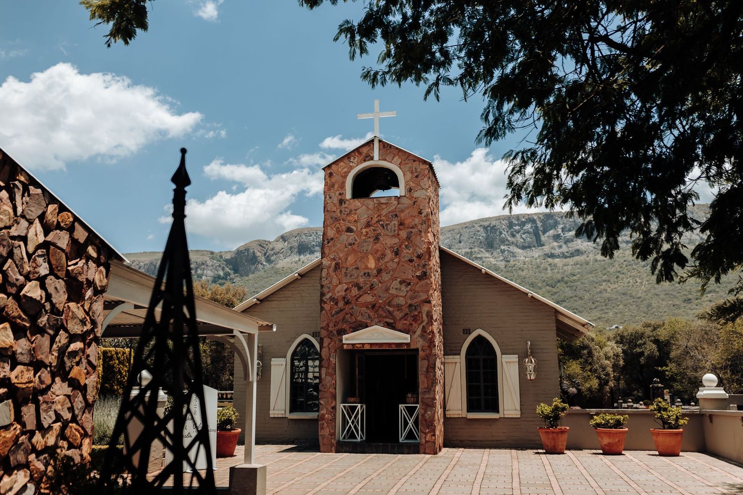 Stone church building with bell tower set against mountains under blue sky.