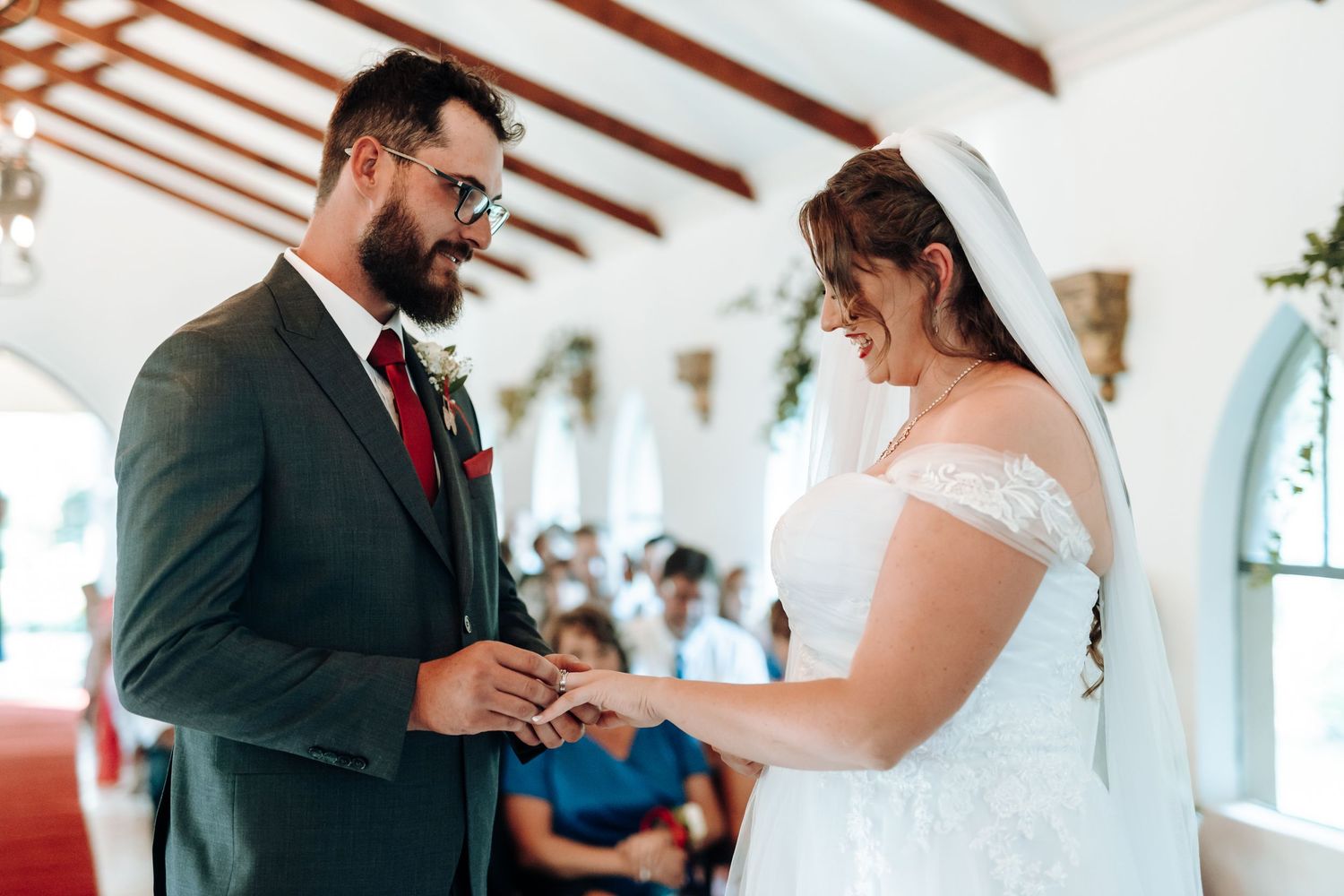 Intimate exchange of rings during a wedding ceremony in a bright chapel with vaulted ceilings.
