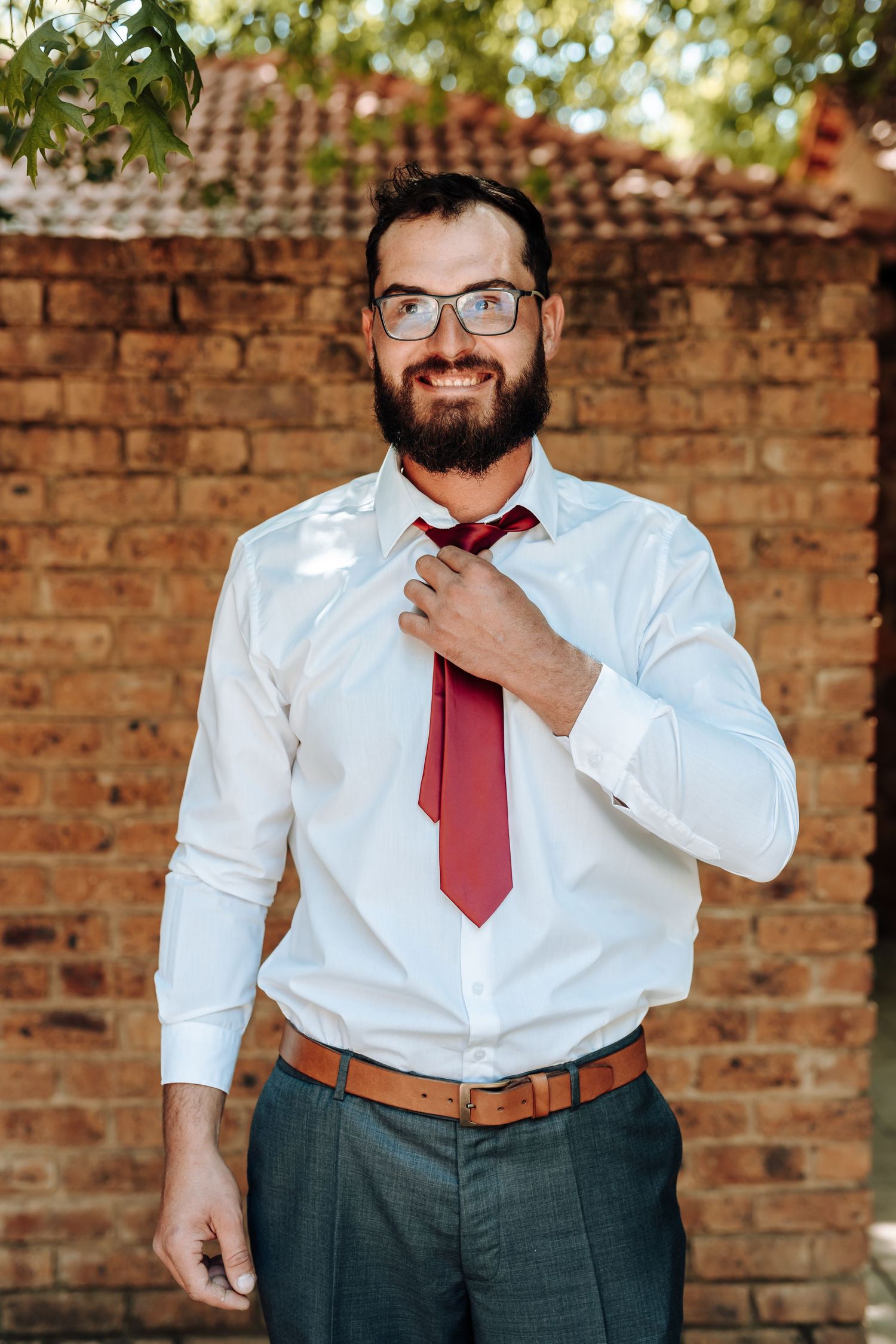 Smart casual business attire with red tie and white shirt against outdoor brick setting.
