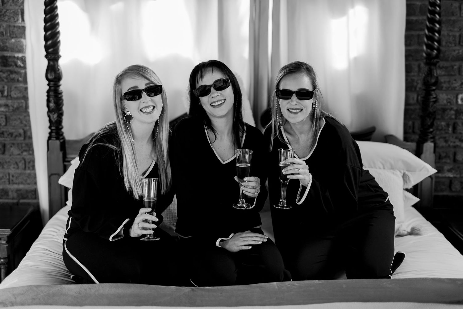 Three friends wearing sunglasses smile while enjoying drinks together in black and white photo.