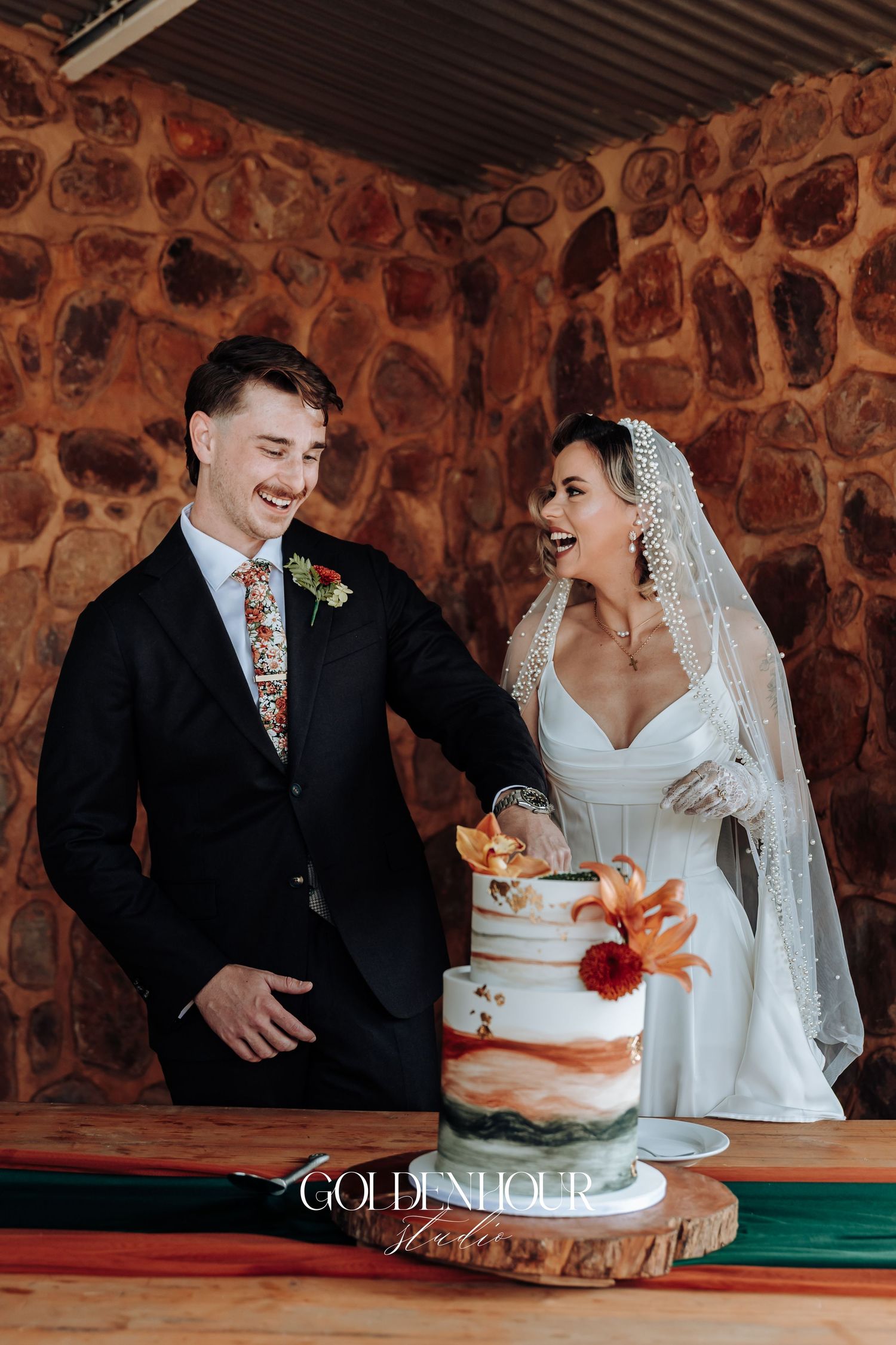 Wedding couple cutting their rustic tiered cake with orange and red floral accents.