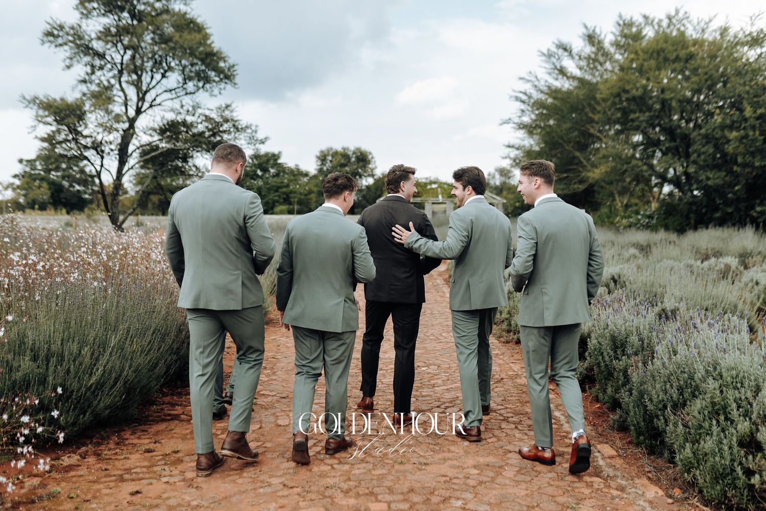 Groomsmen in sage green suits walking together on a garden path.
