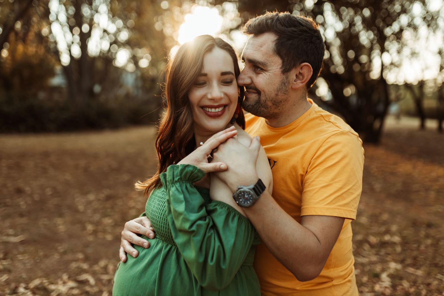 A romantic couple laughs and embraces outdoors during golden hour in a casual autumn photoshoot.