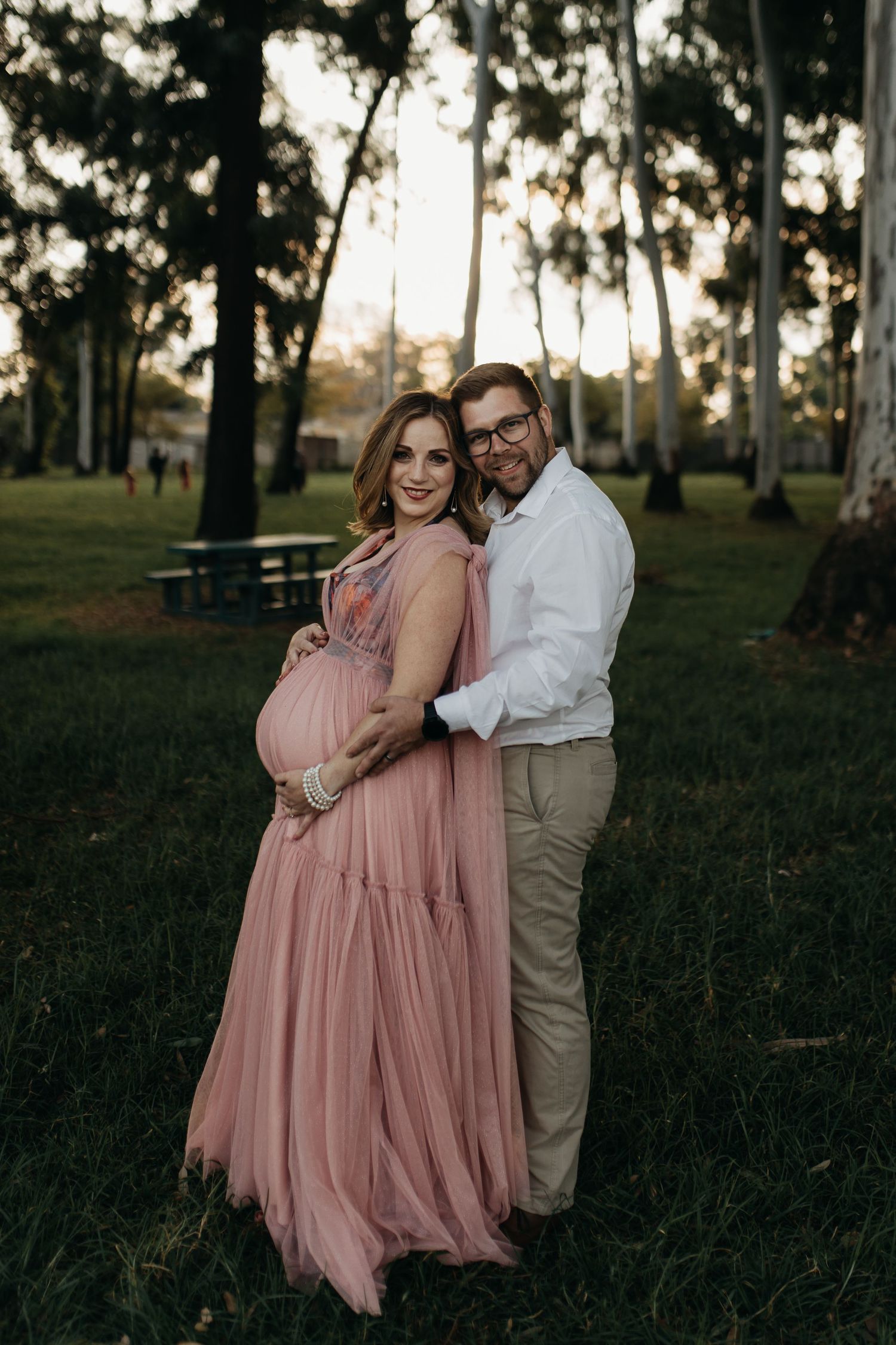 Family standing together in a grassy field at sunset wearing pink dresses and casual attire.