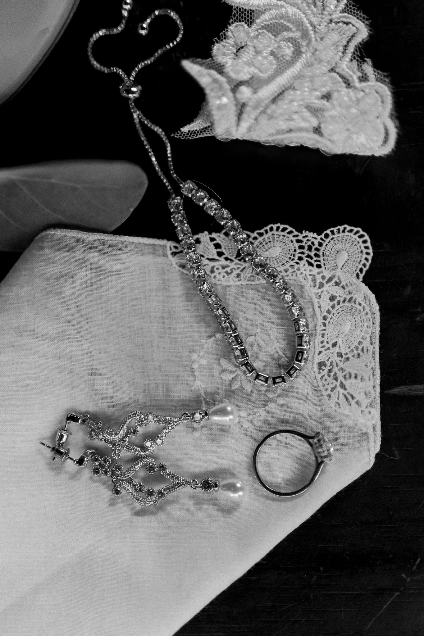 Black and white detail shot of wedding jewelry and accessories on white linen.