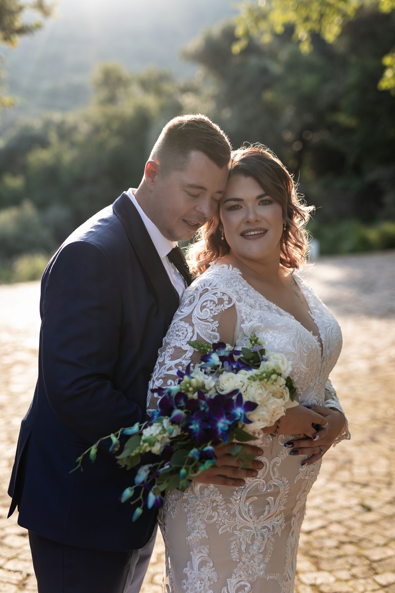 Happy couple poses with vibrant blue and white wedding bouquet on scenic overlook.