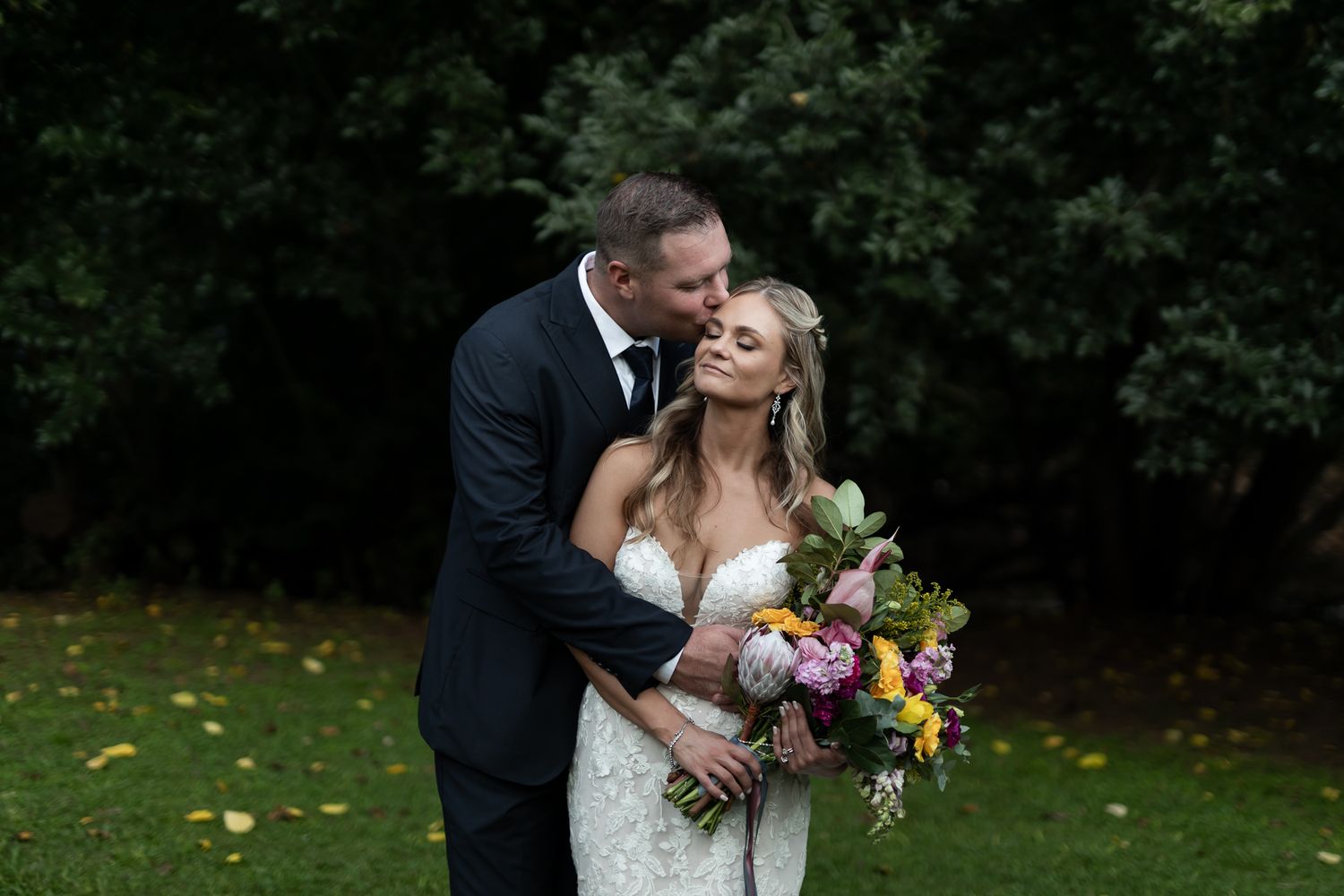 Joyful couple shares romantic moment outdoors while bride holds vibrant bouquet.