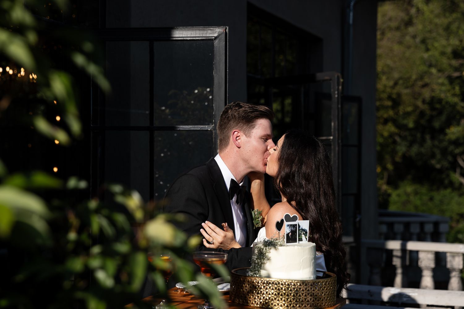 A newly married couple shares cake together at their outdoor wedding reception.