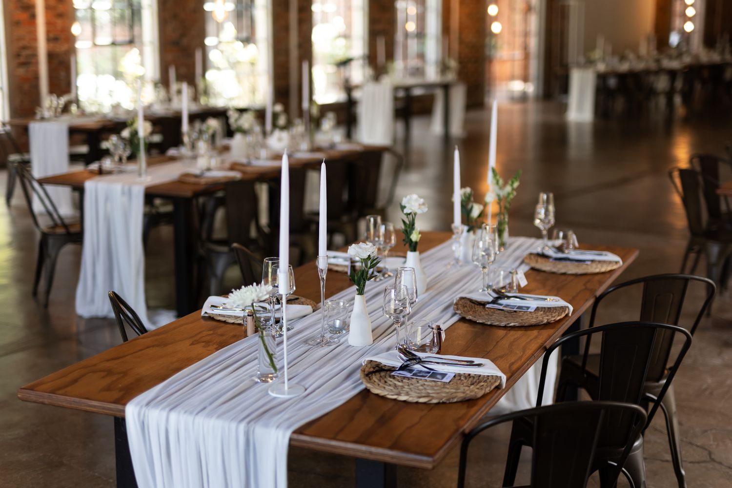 Modern rustic wedding reception tables with white runners, candles and elegant place settings.