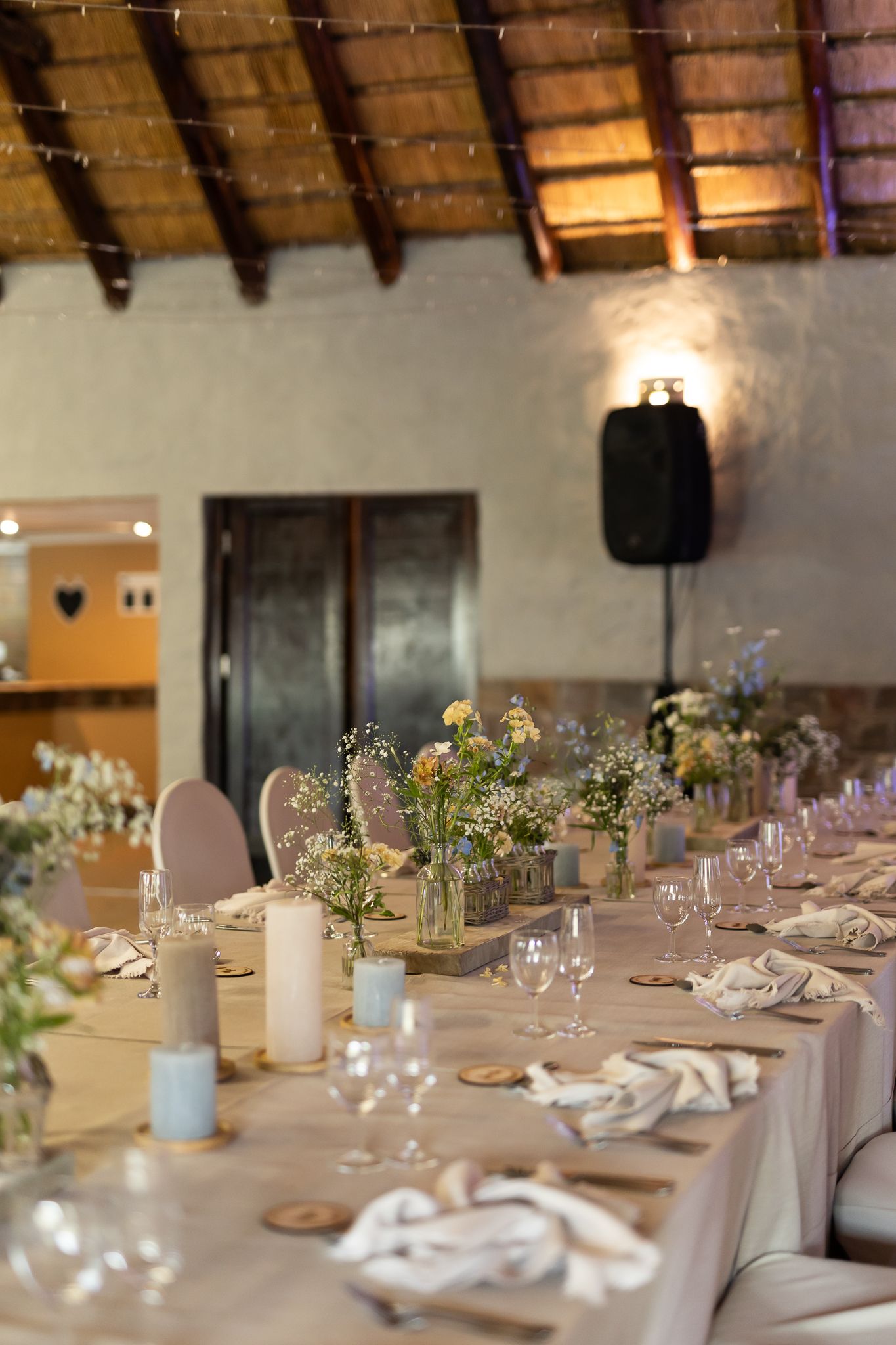 Rustic wedding reception table with wild flower centerpieces under exposed wooden beams.