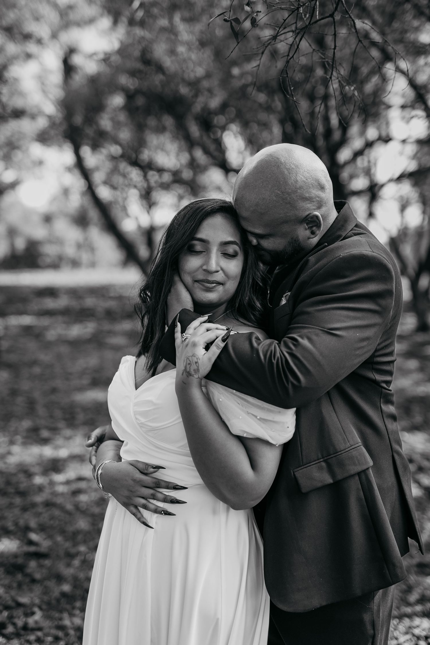 A black and white photo captures an intimate moment between newlyweds embracing outdoors.