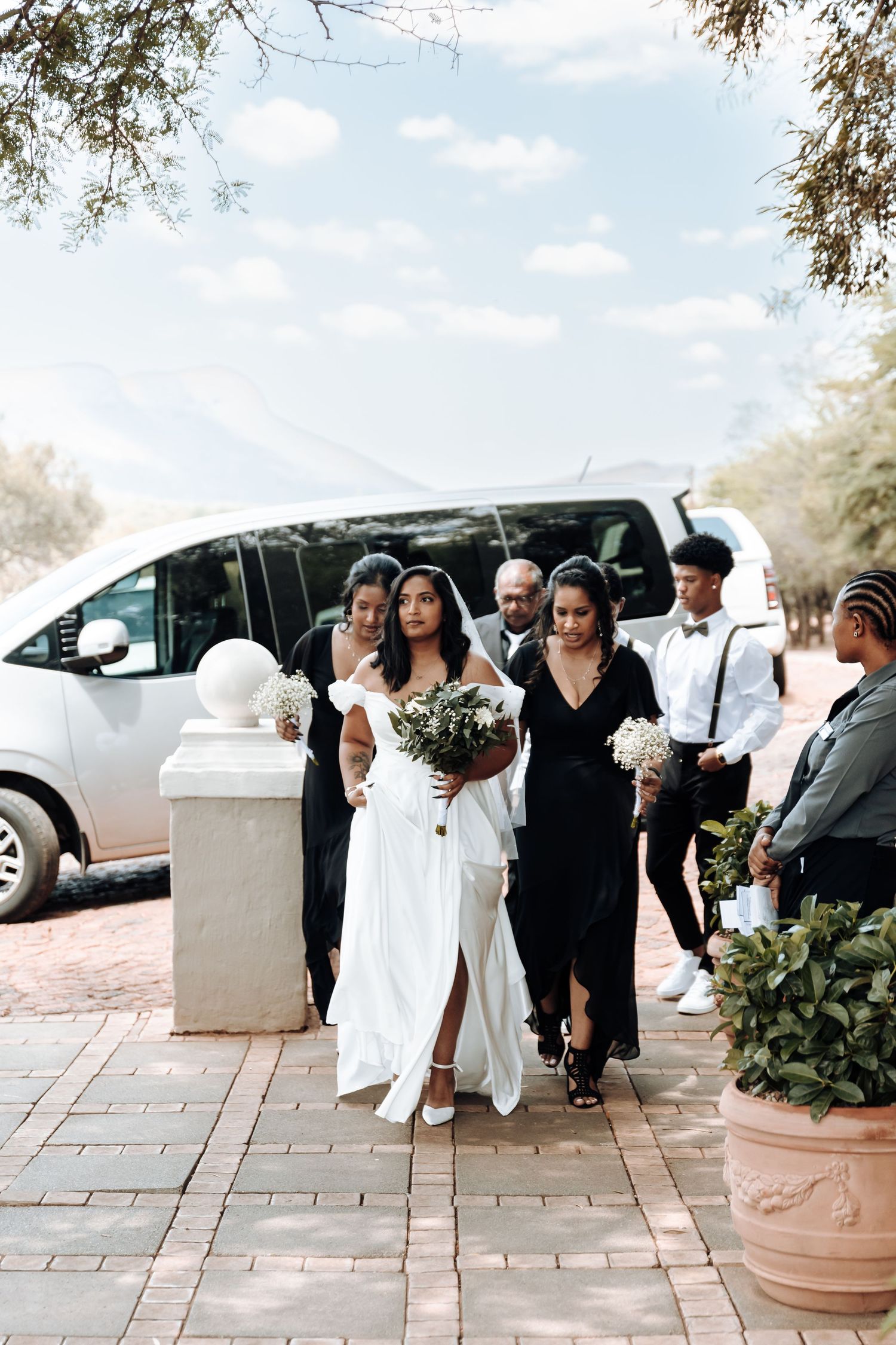Wedding party arriving at venue with bridal party in black dresses and white gown.
