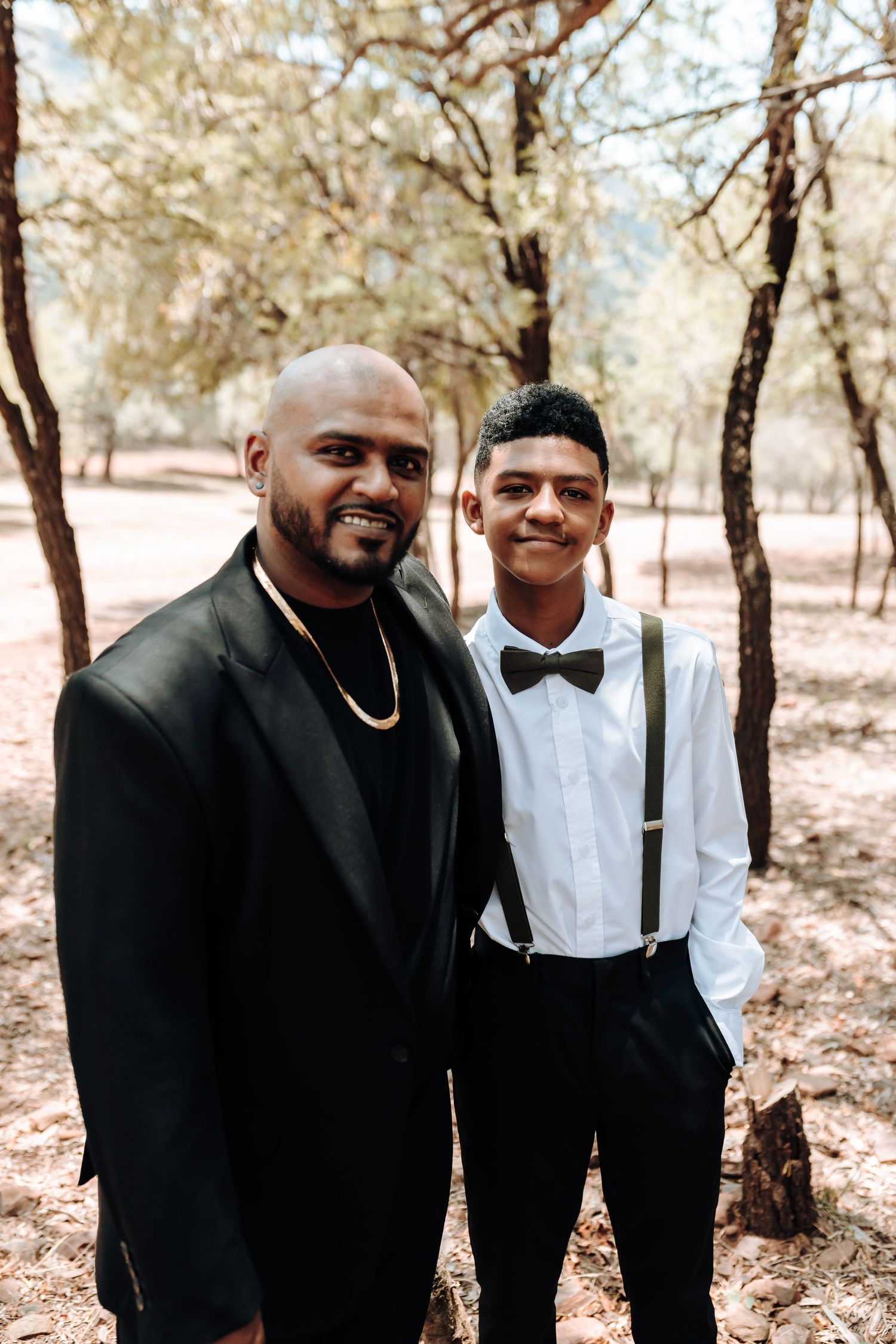 Two people in formal wear smiling together in outdoor woodland setting.