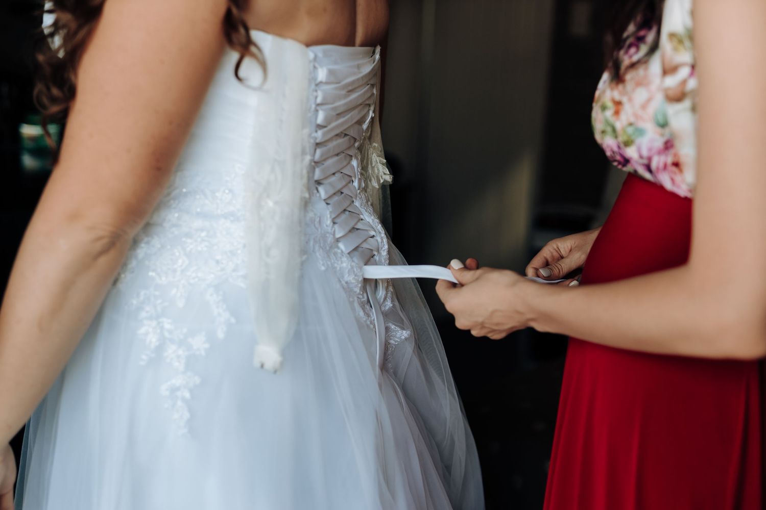 Close-up detail of wedding dress being laced up from behind.