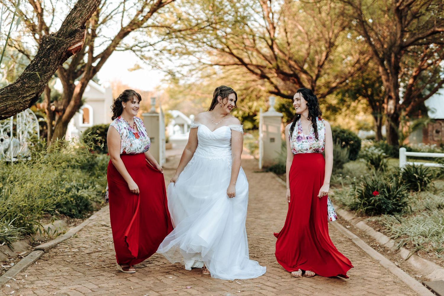 Wedding party wearing red and white dresses stand together on brick pathway.