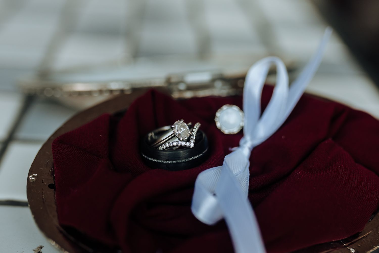 Elegant diamond engagement ring displayed on deep red velvet with white ribbon accent.