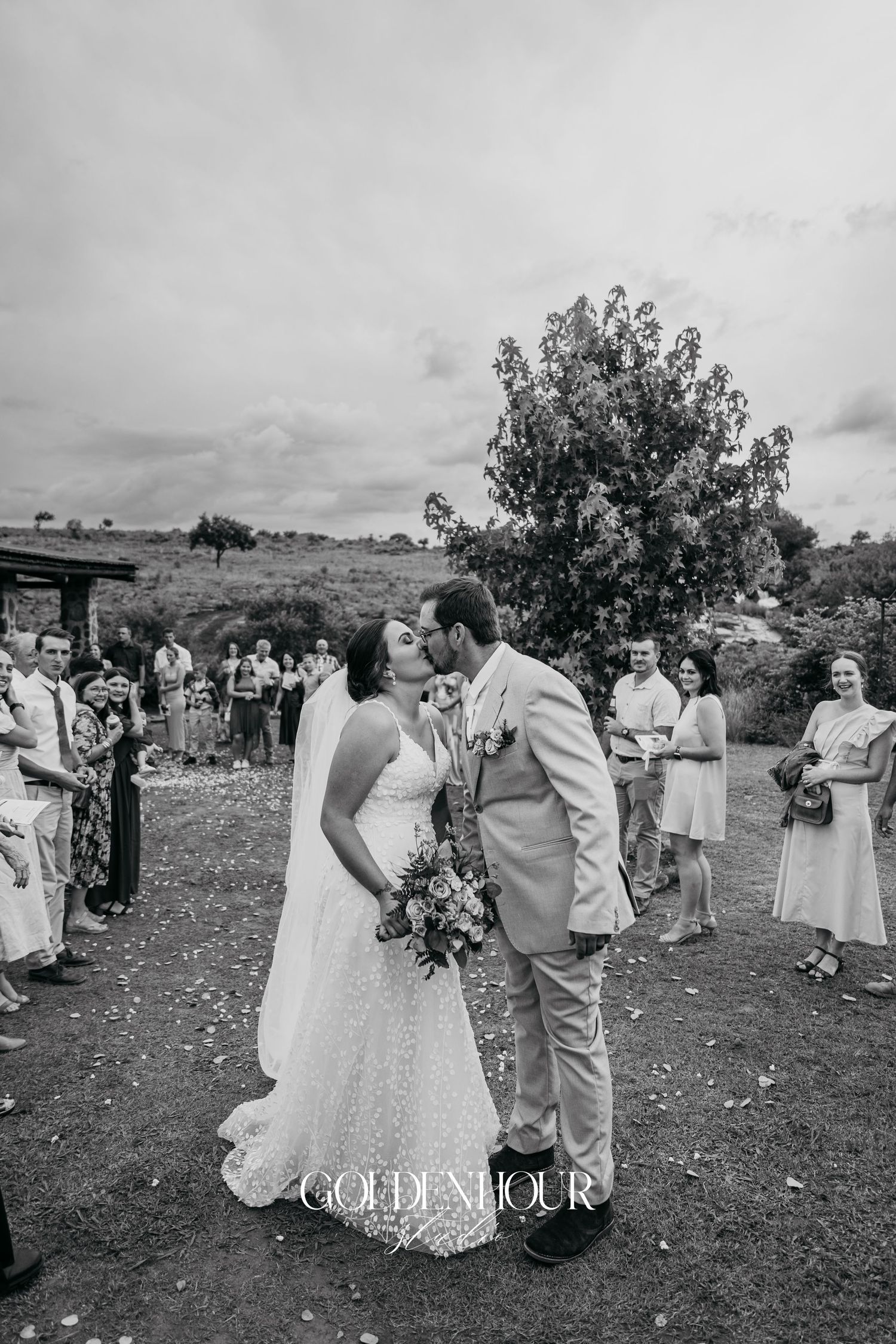 Wedding couple sharing a dance surrounded by guests on a cloudy day.