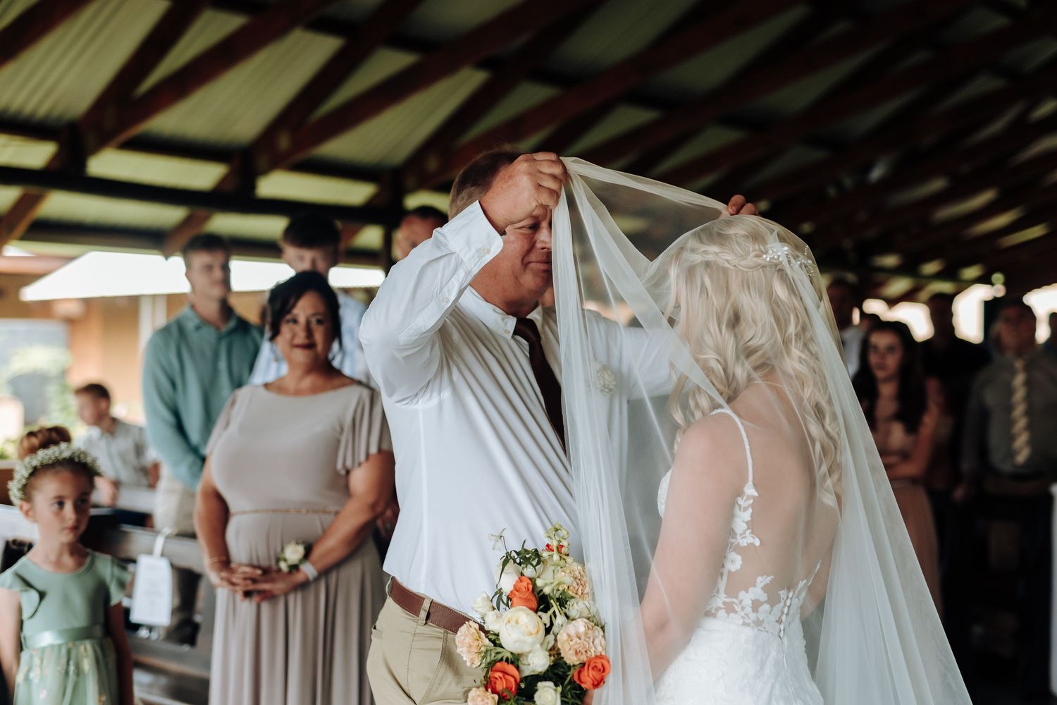A wedding party poses together in a rustic barn setting with elegant white and mint green attire.
