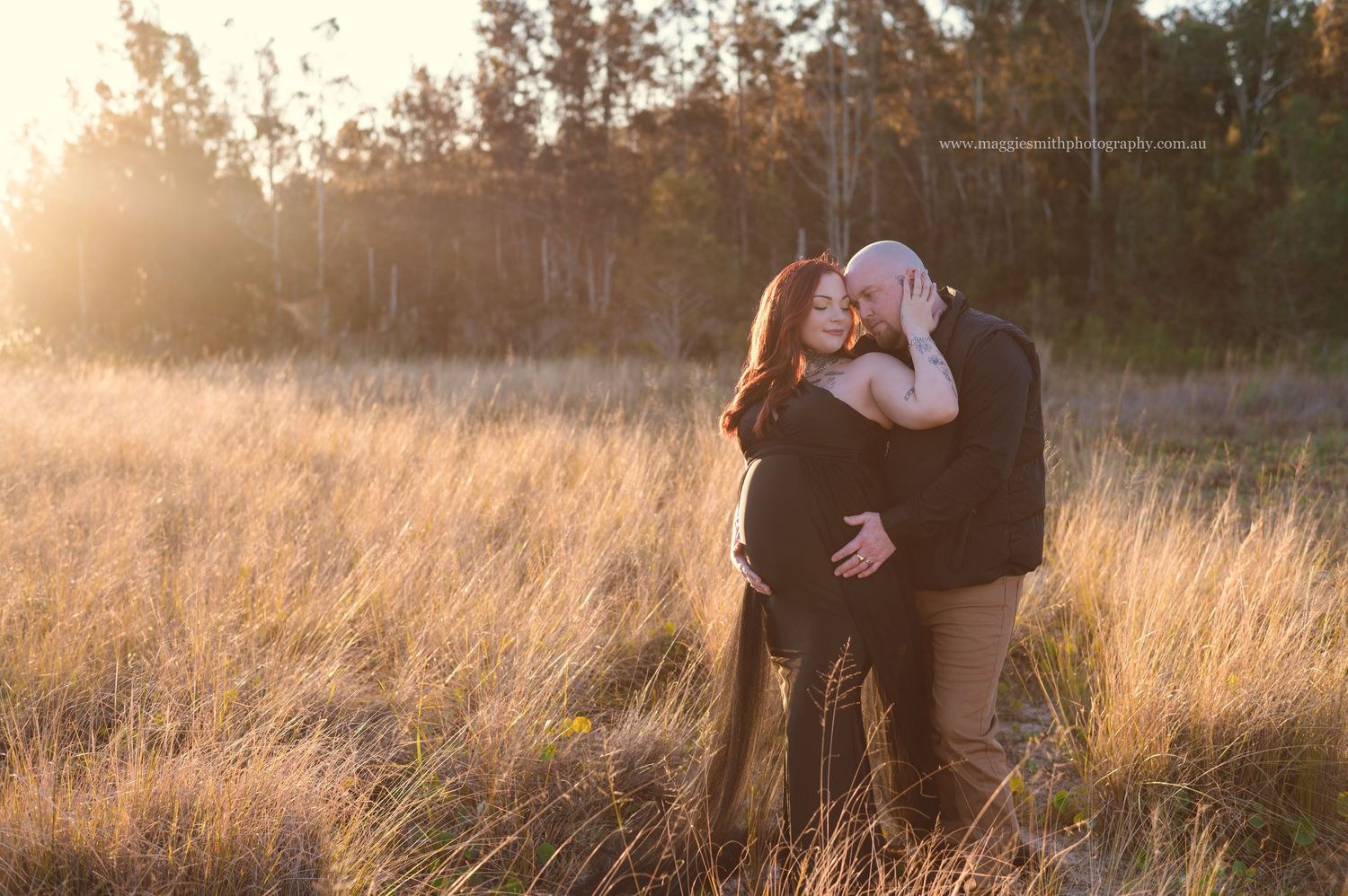 A pregnant couple embraces in a golden sunlit field during sunset creating a romantic silhouette against the warm glowing sky. Maternity.