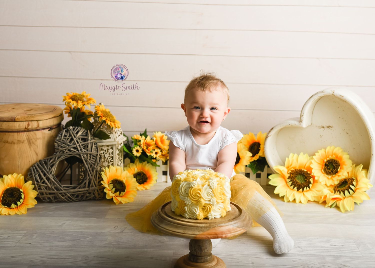 Yellow sunflower themed cake smash photography setup with rustic decorations on white wood background.